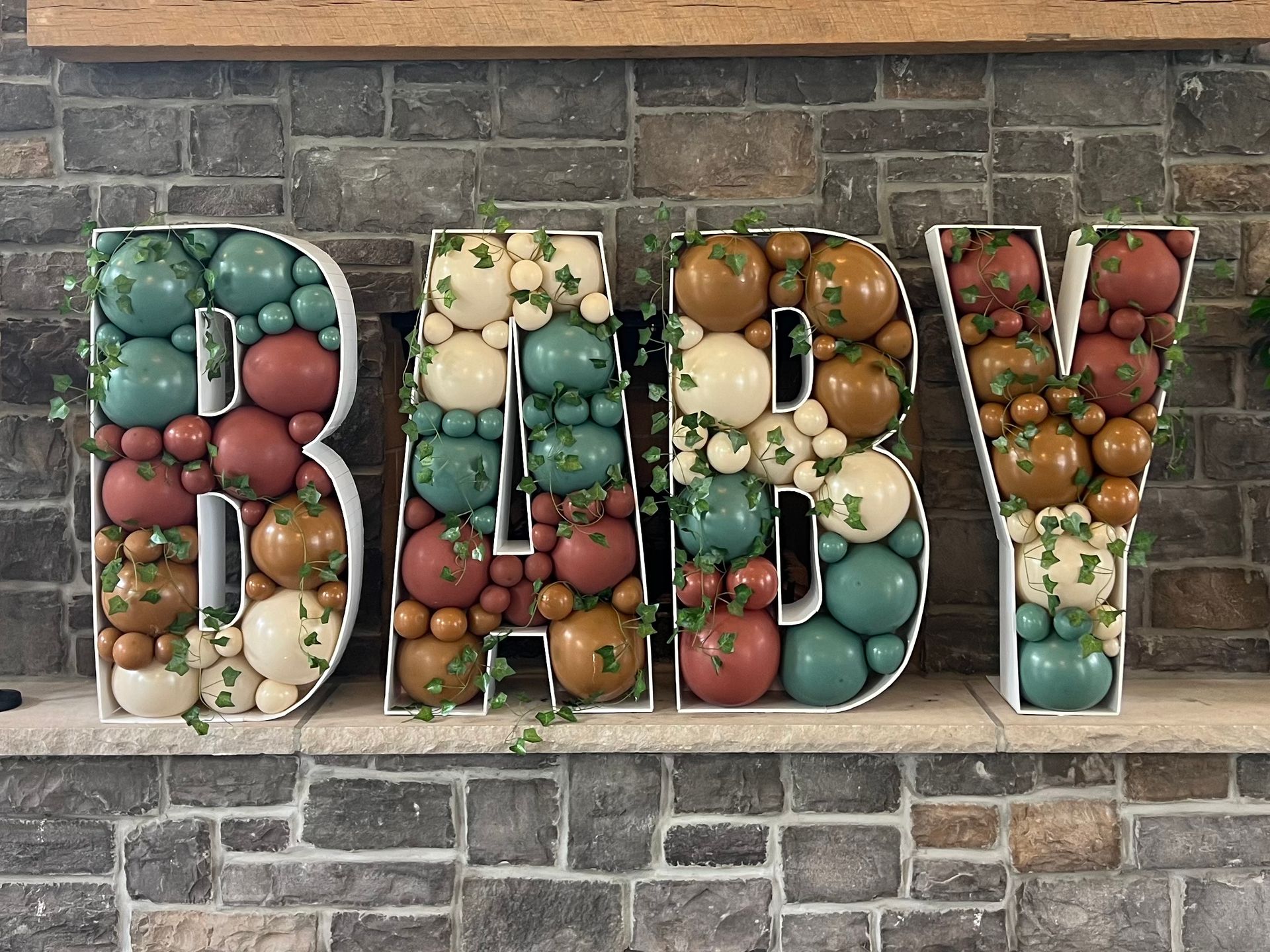 The word baby is made out of balloons on a mantle.
