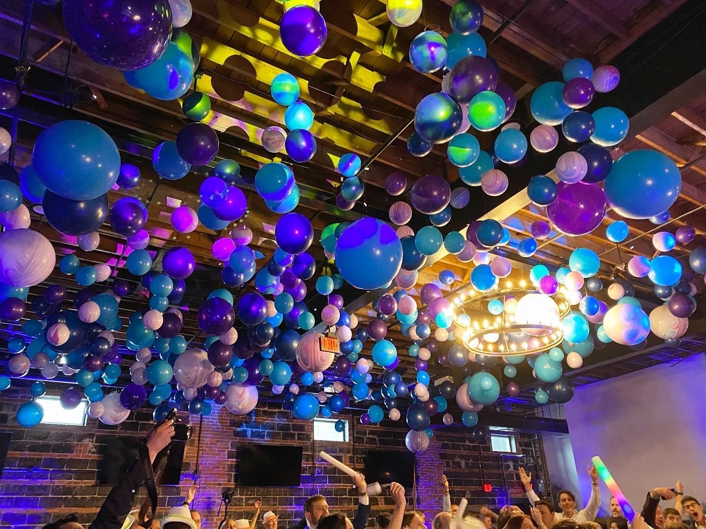 A crowd of people are dancing in a room with balloons hanging from the ceiling.