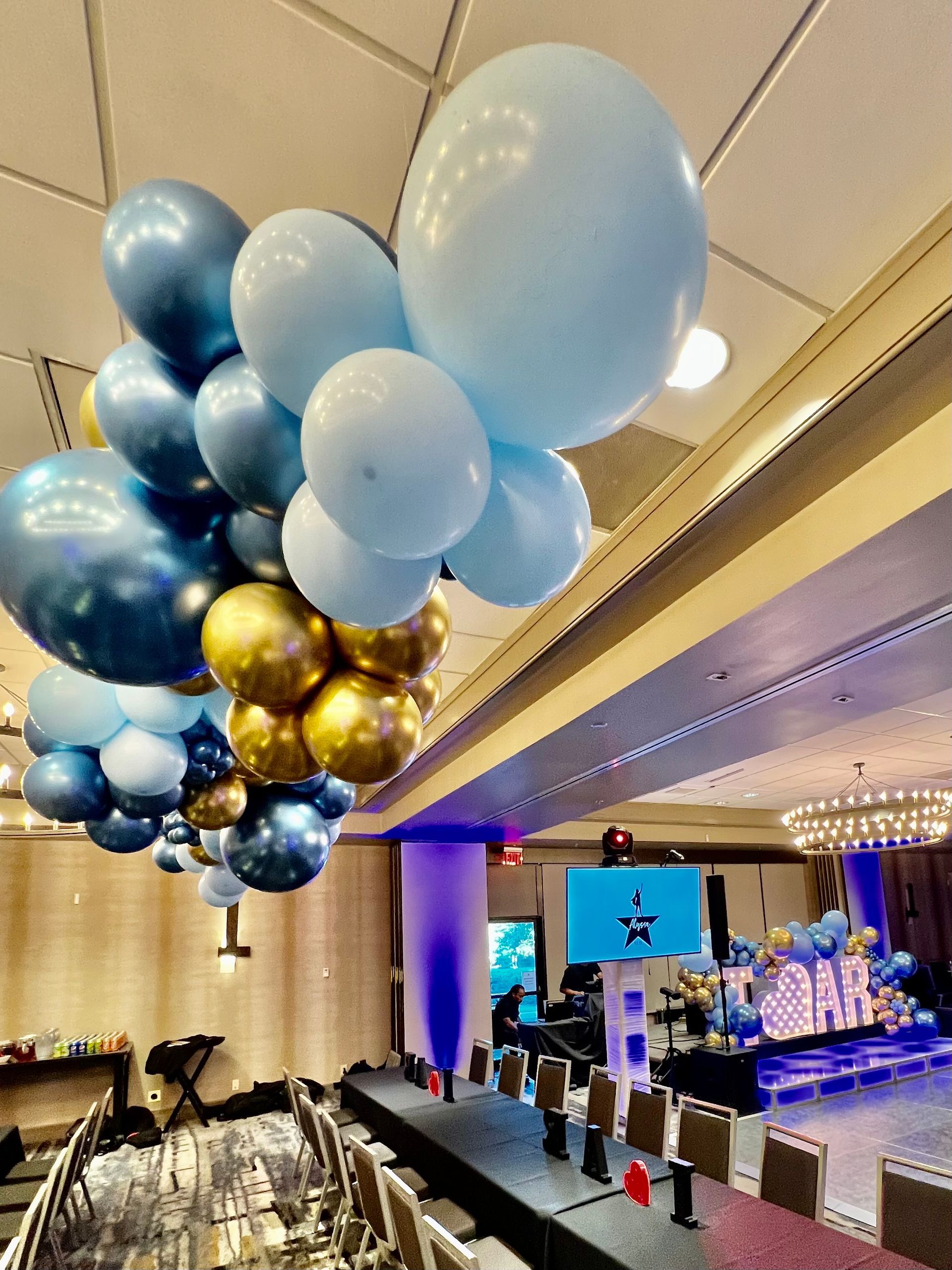 A bunch of blue and gold balloons are hanging from the ceiling of a room.
