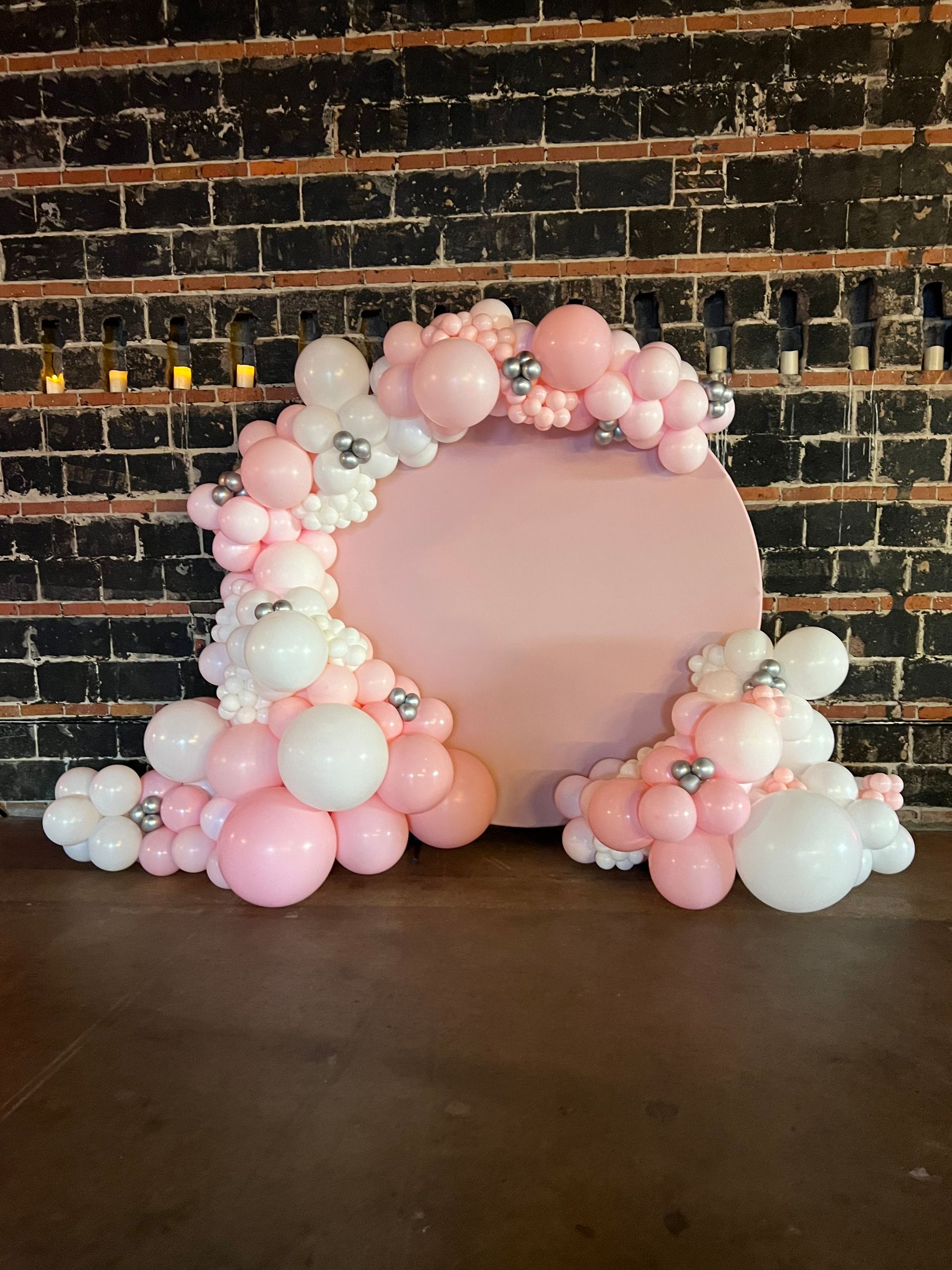 A pink and white balloon arch is sitting in front of a brick wall.
