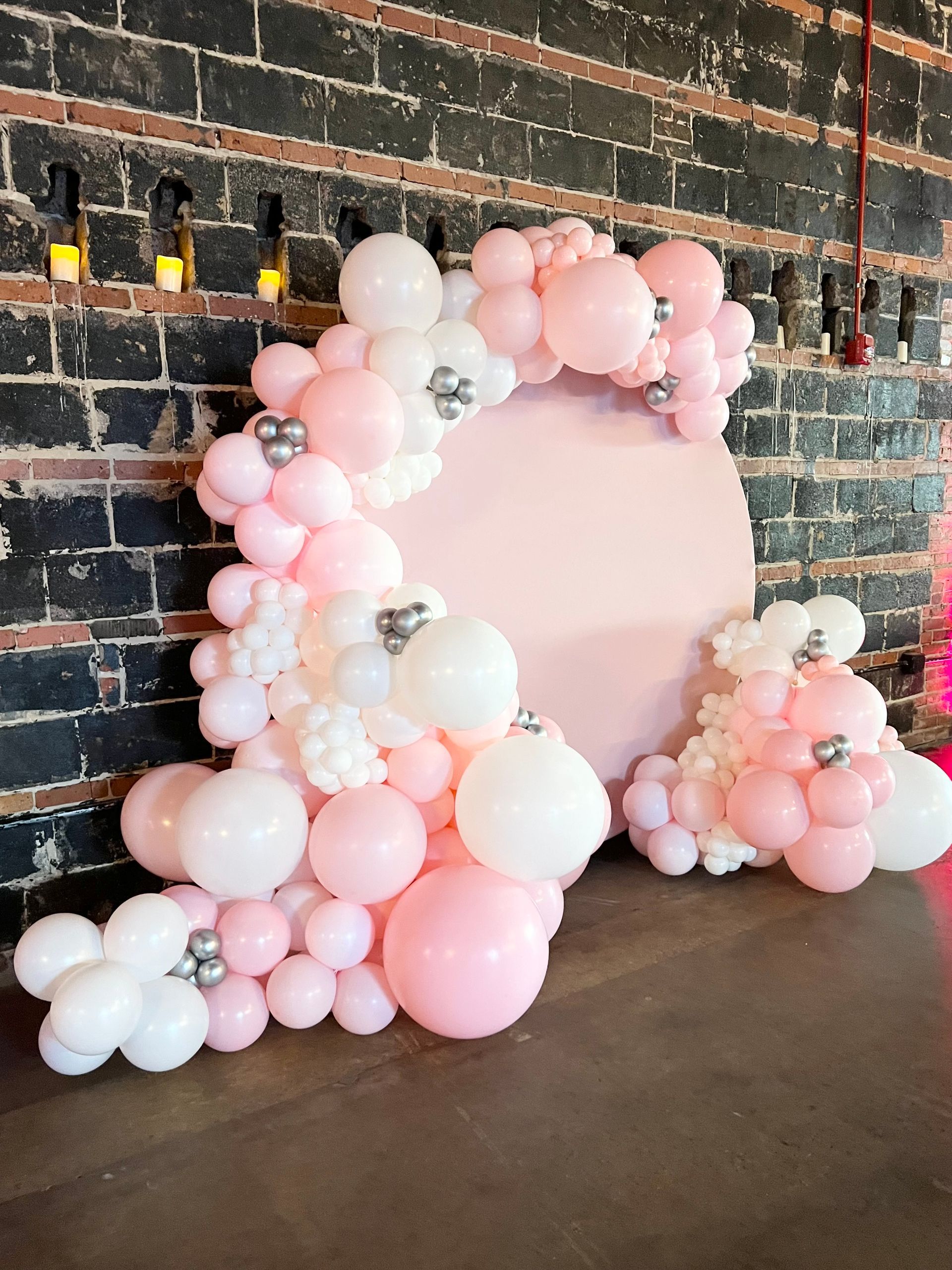 A bunch of pink and white balloons are sitting in front of a brick wall.
