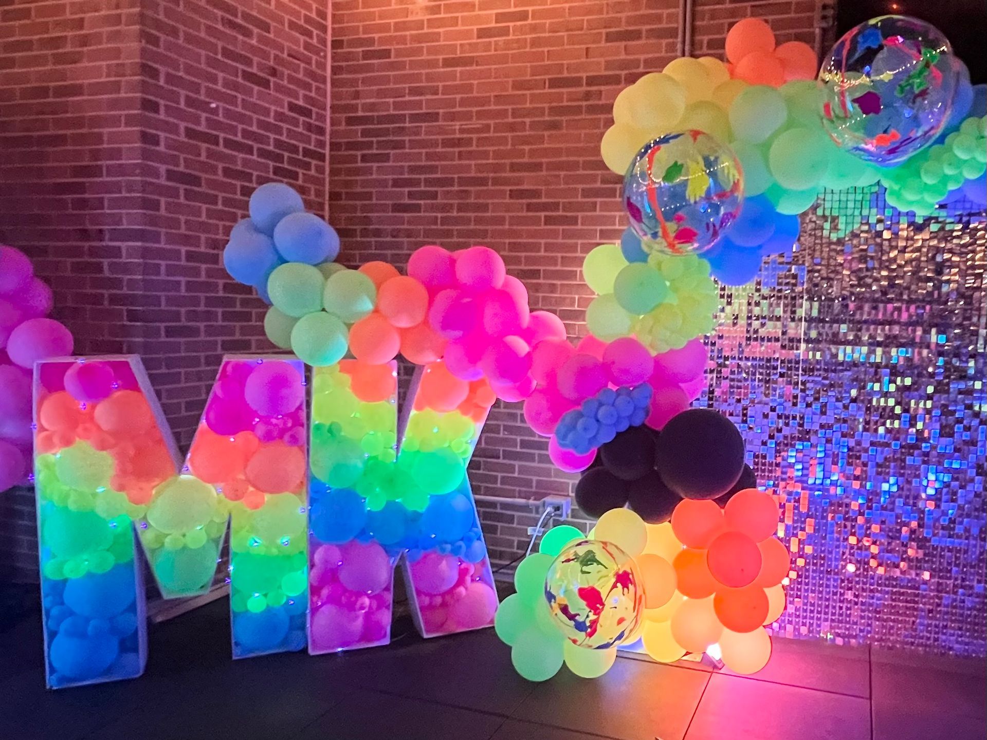 A large letter m is surrounded by glow in the dark balloons.
