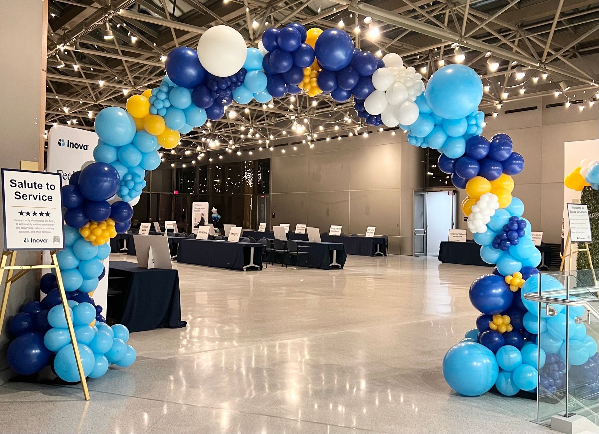 A large room decorated with blue , white and yellow balloons.