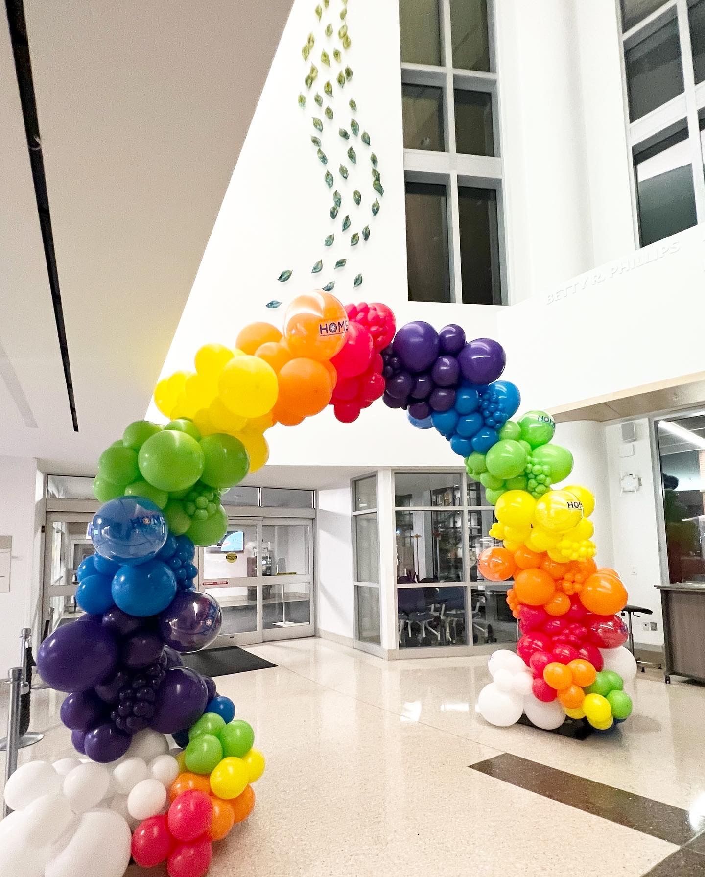 A rainbow colored balloon arch in a hallway.