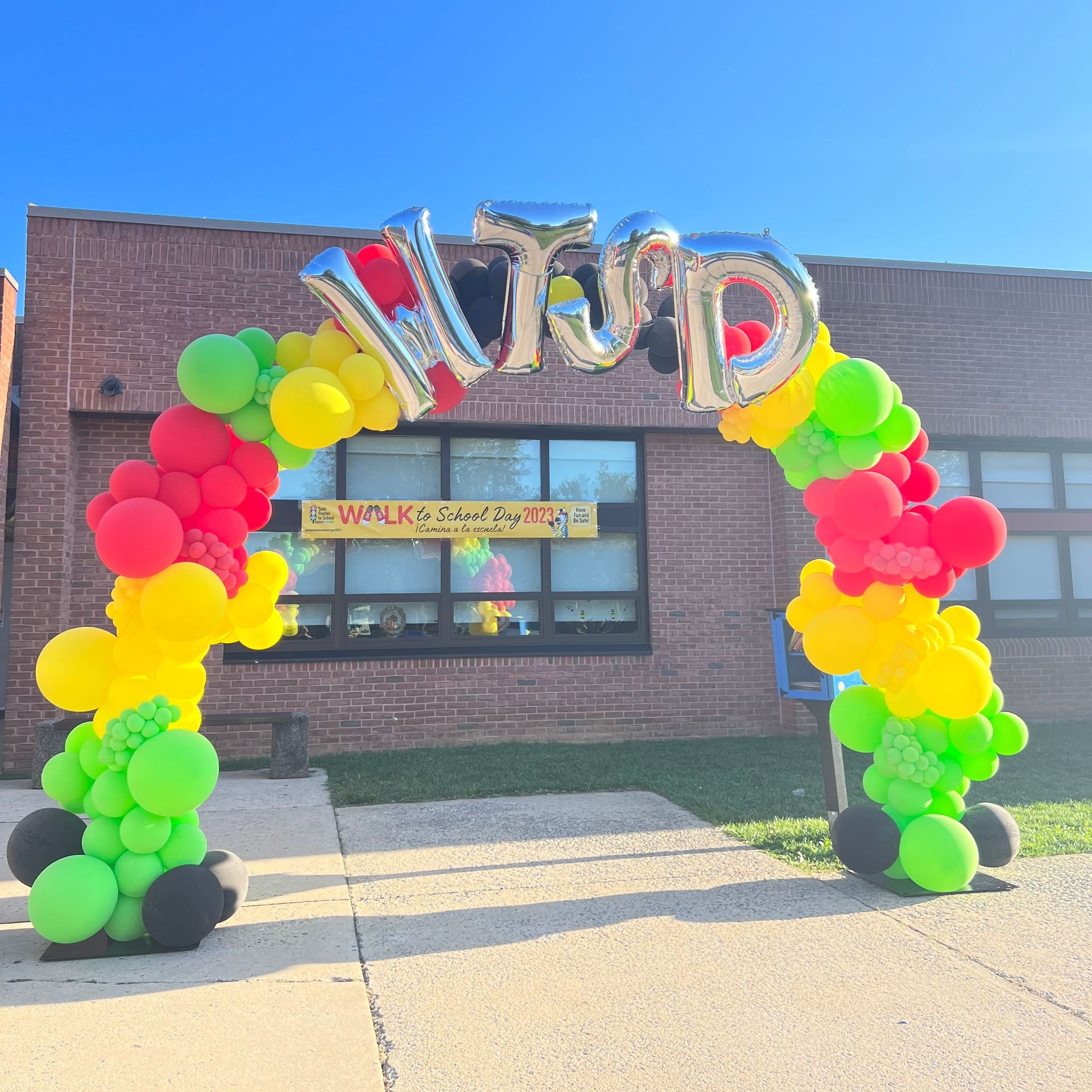 A colorful balloon arch is in front of a brick building.