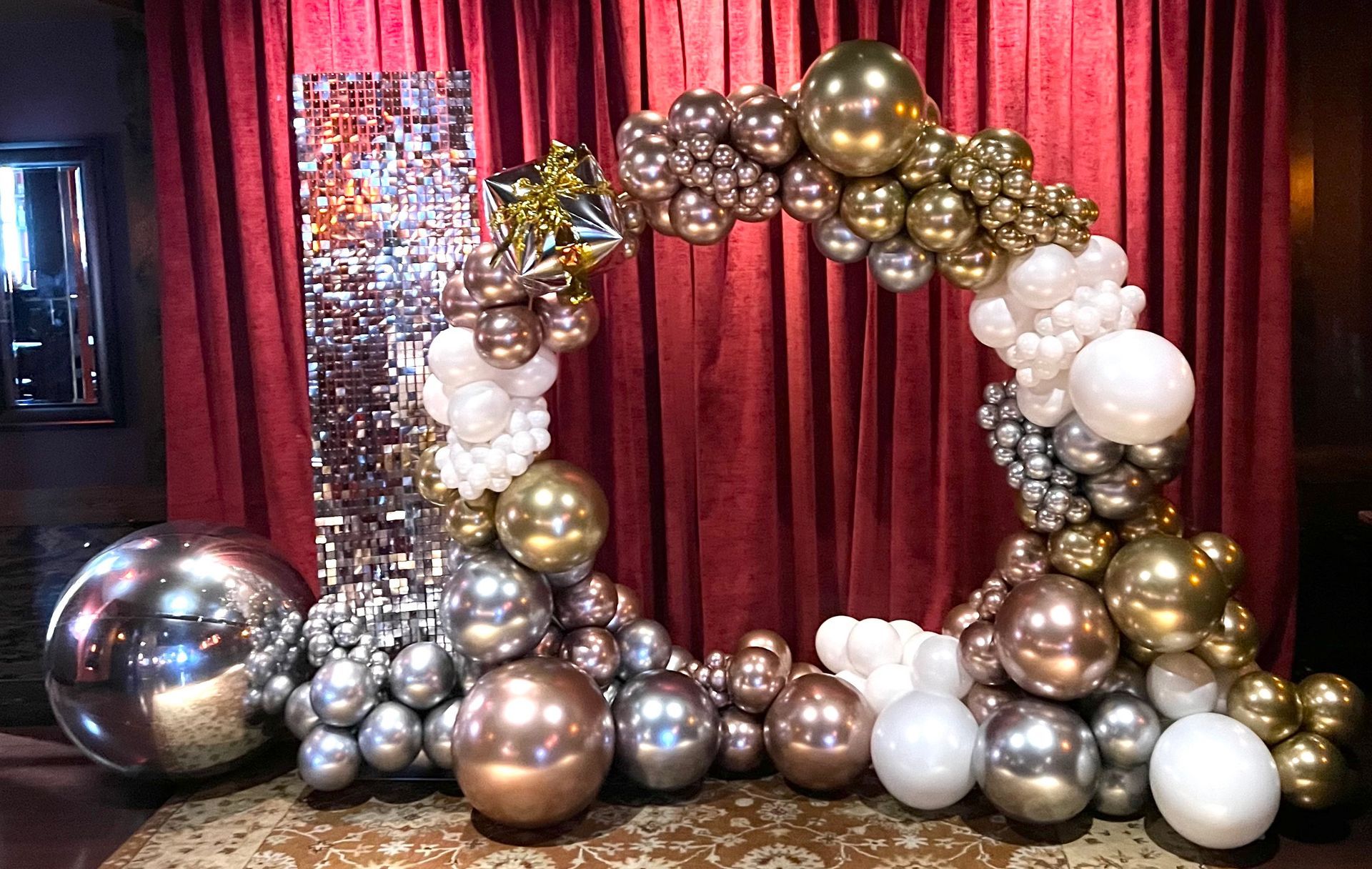 A bunch of balloons are sitting in front of a red curtain.