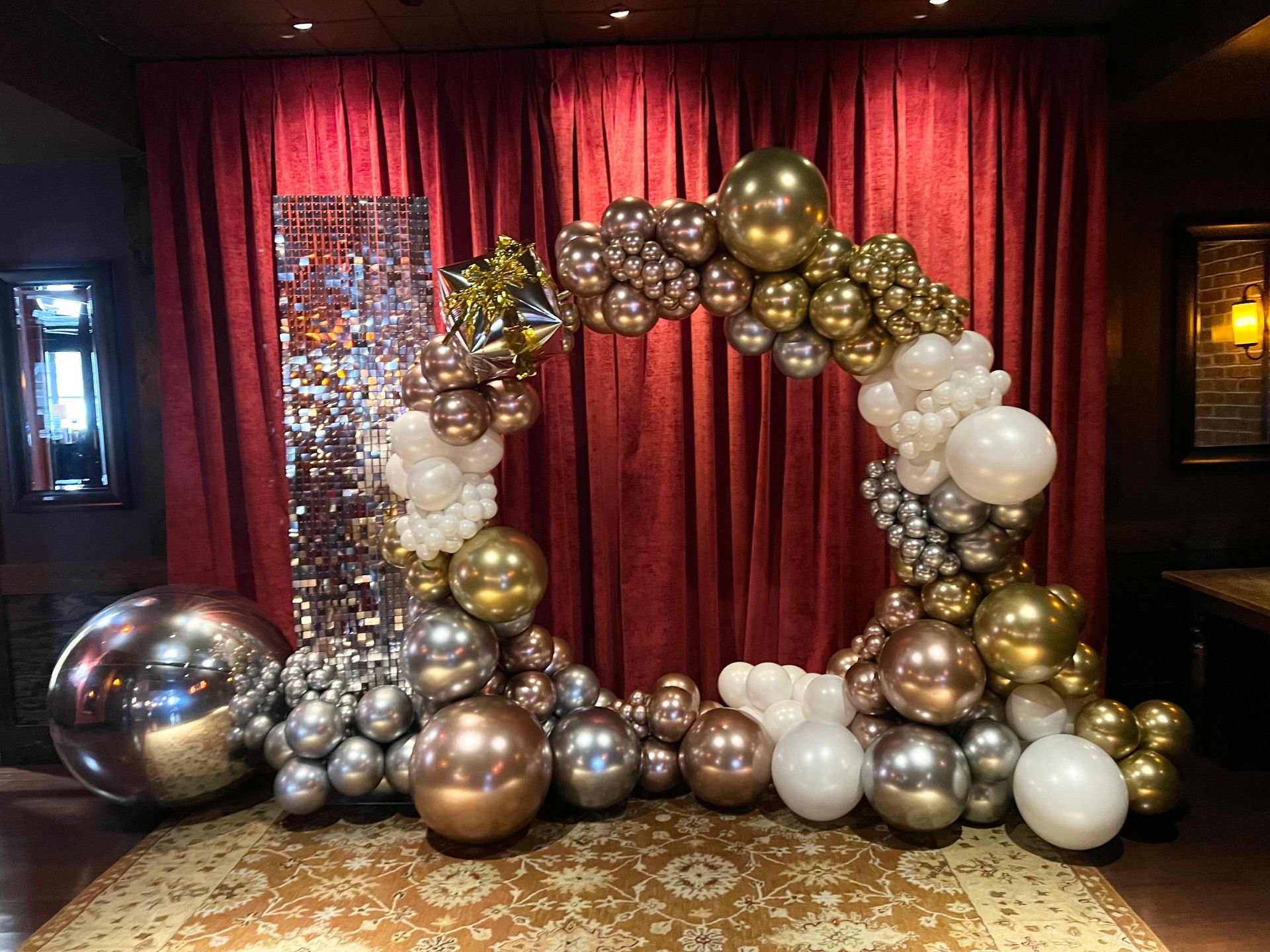 A balloon arch is sitting in front of a red curtain in a room.