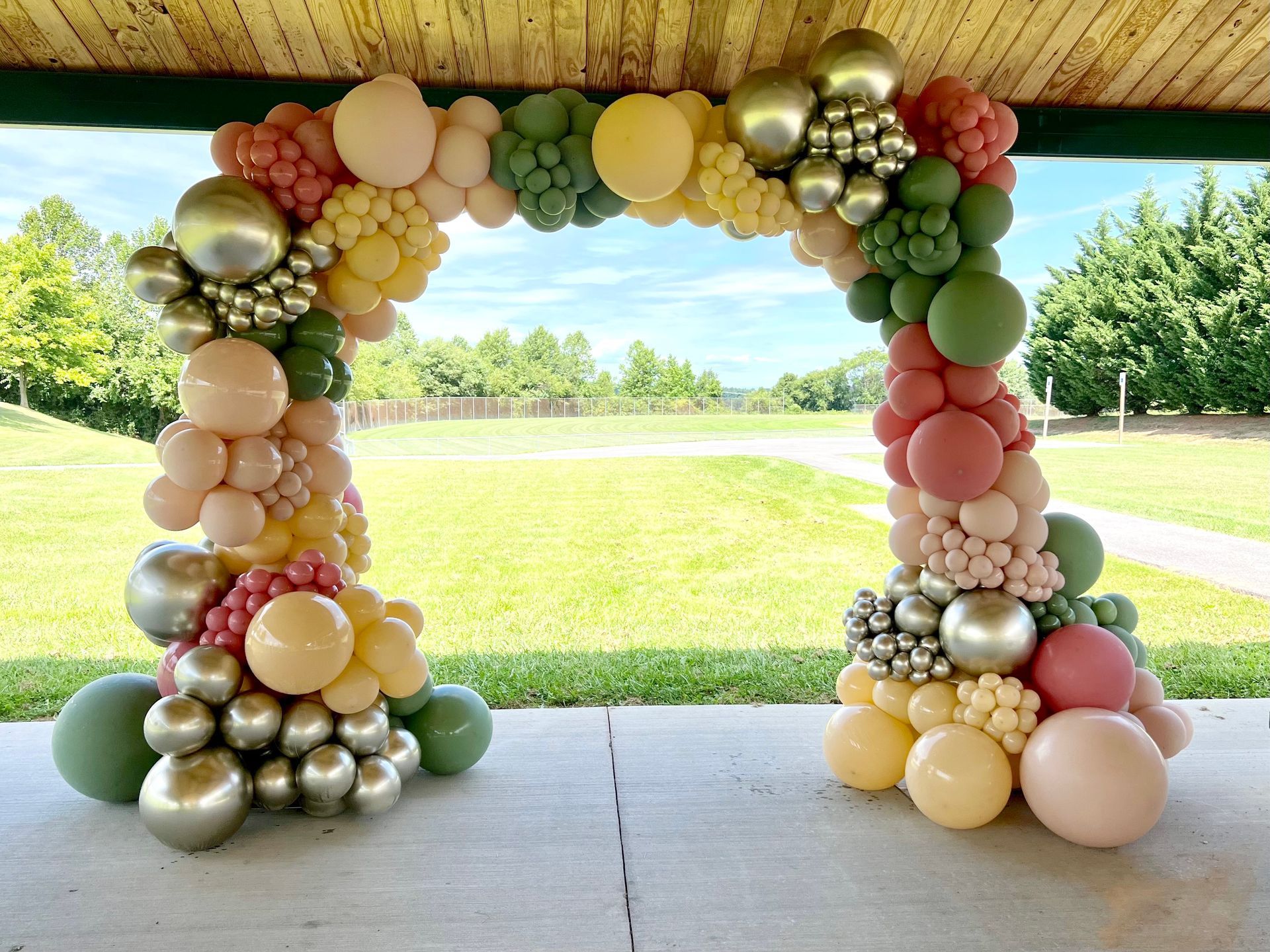 A large arch made of balloons is sitting on the ground in a park.