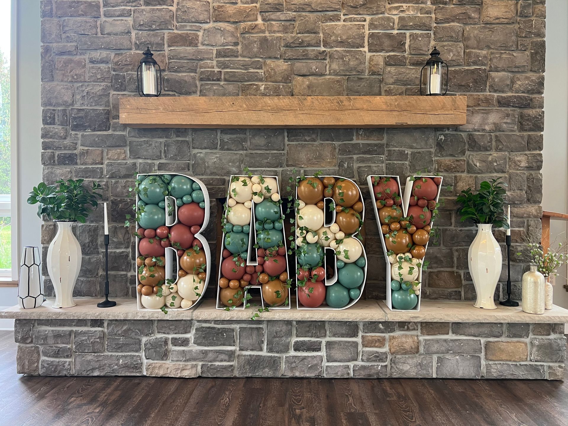 A fireplace decorated for a baby shower with the word baby made out of balloons.