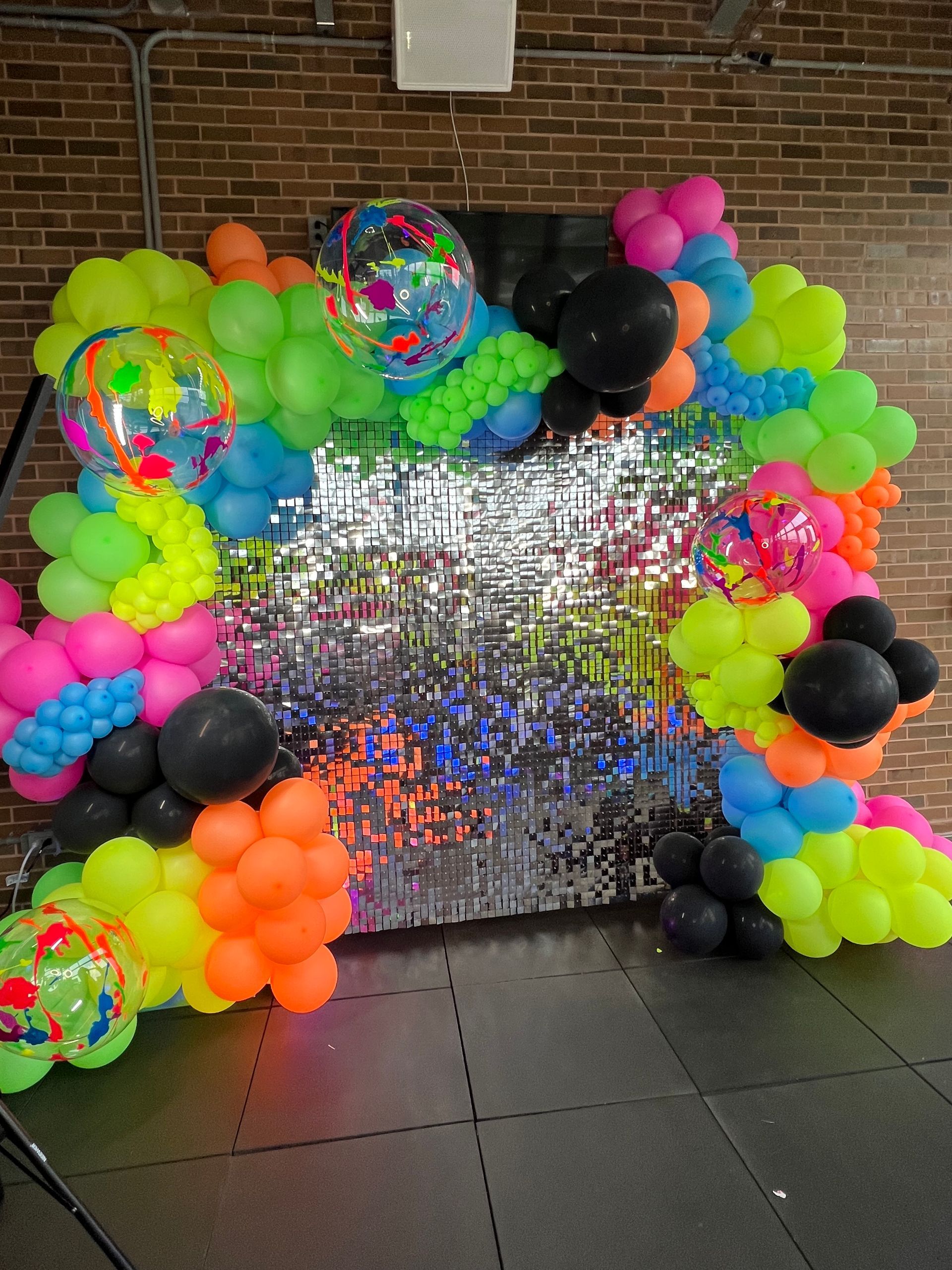 A bunch of colorful balloons are sitting on the floor in front of a brick wall.