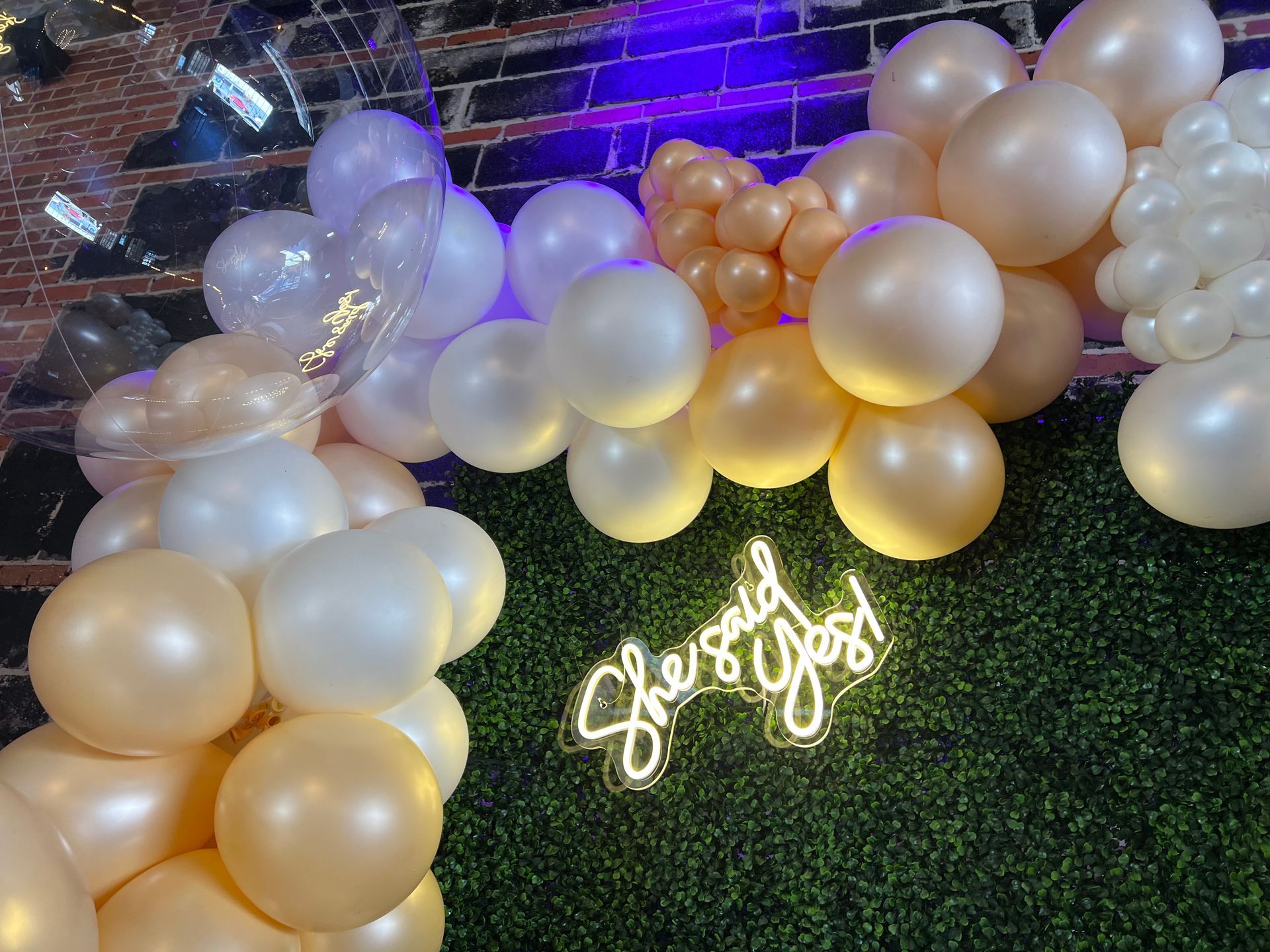 A bunch of balloons and a neon sign on a wall.