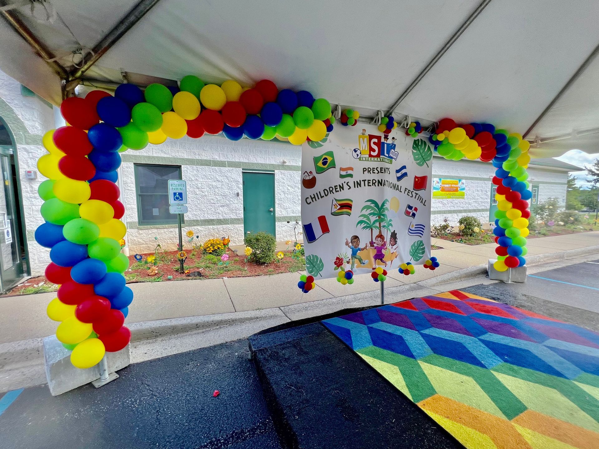 A tent is decorated with colorful balloons and a rainbow rug.