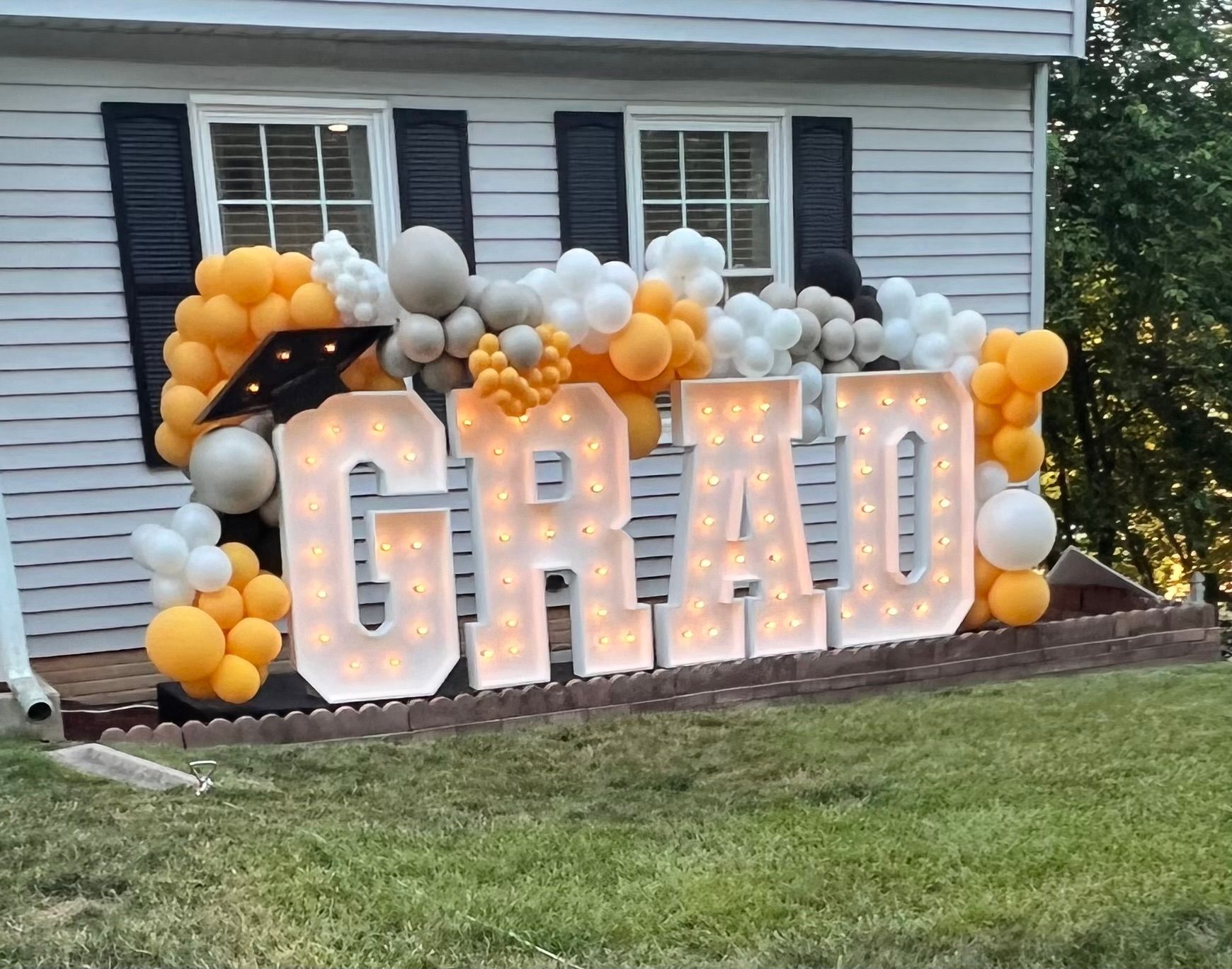 A sign that says `` grad '' is surrounded by balloons in front of a house.