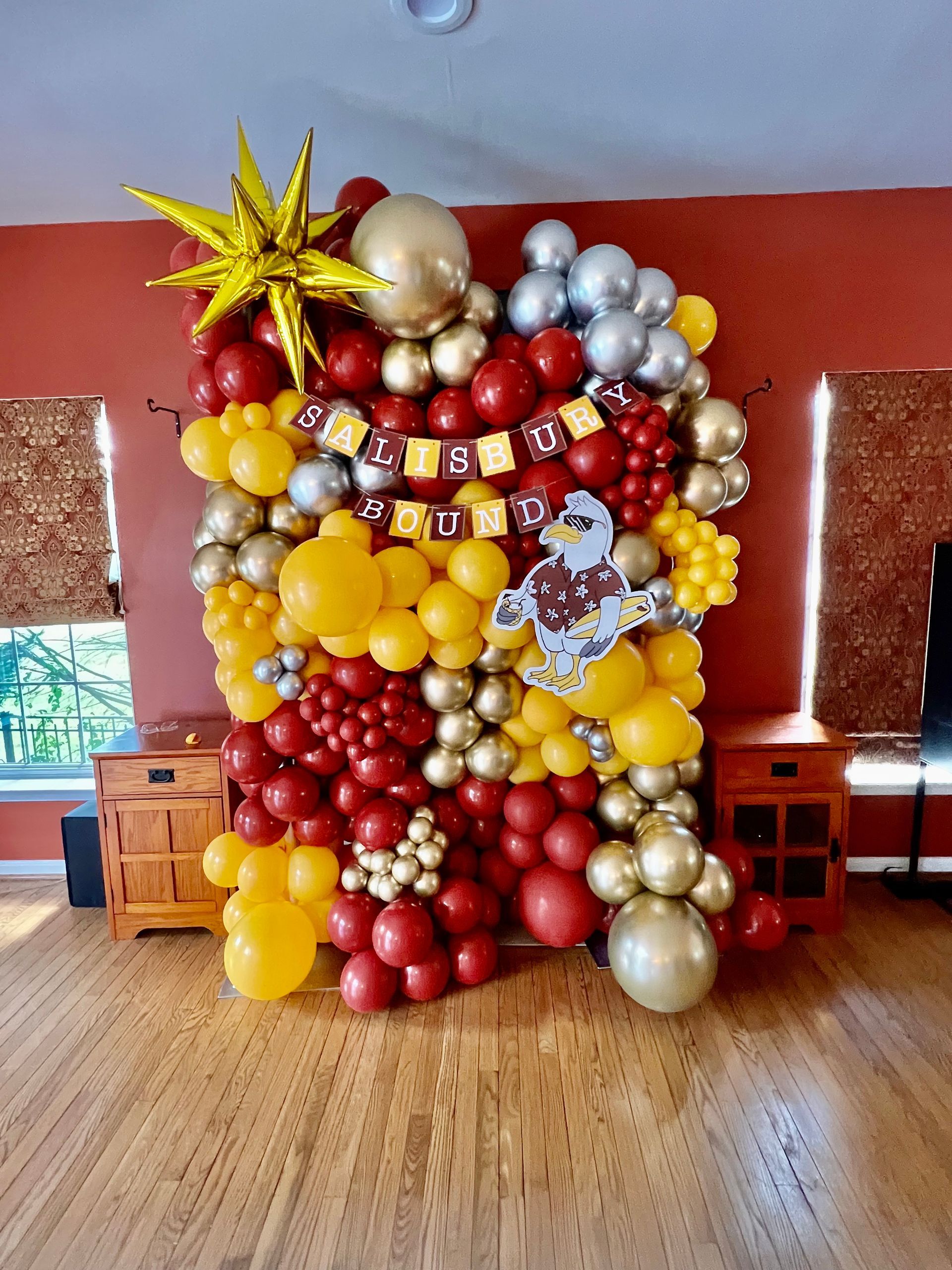 A wall of red , yellow , and gold balloons in a room.