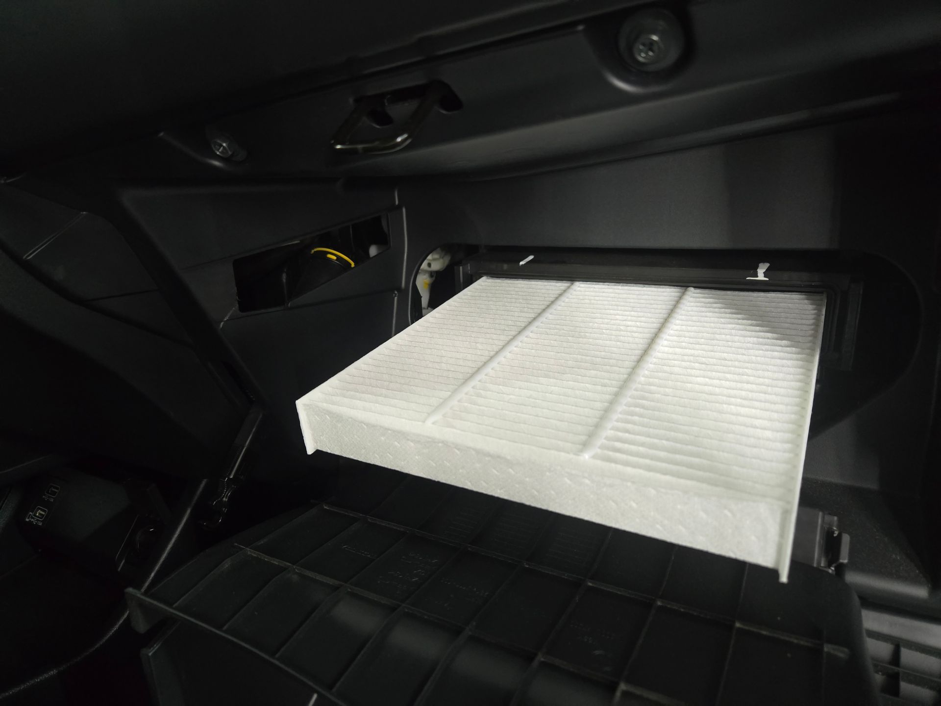 A car's open glove compartment with a white cabin air filter being replaced.