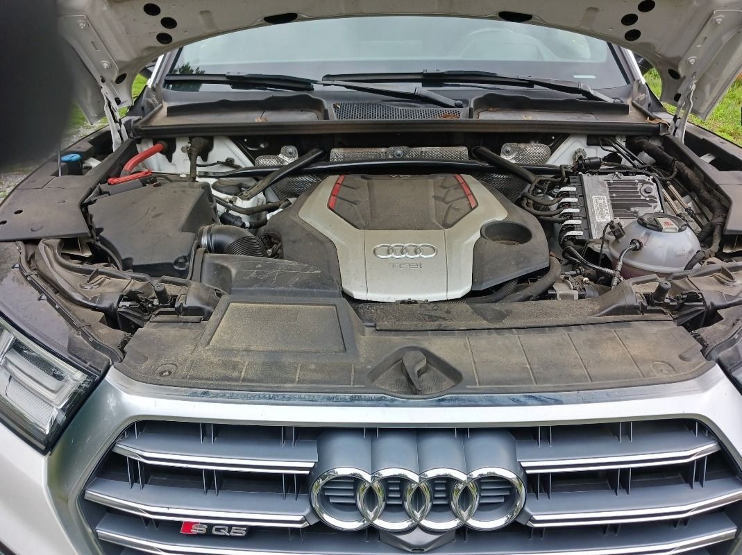 Audi SQ5 engine compartment, hood open, gray engine cover, silver grille with rings, dirt.