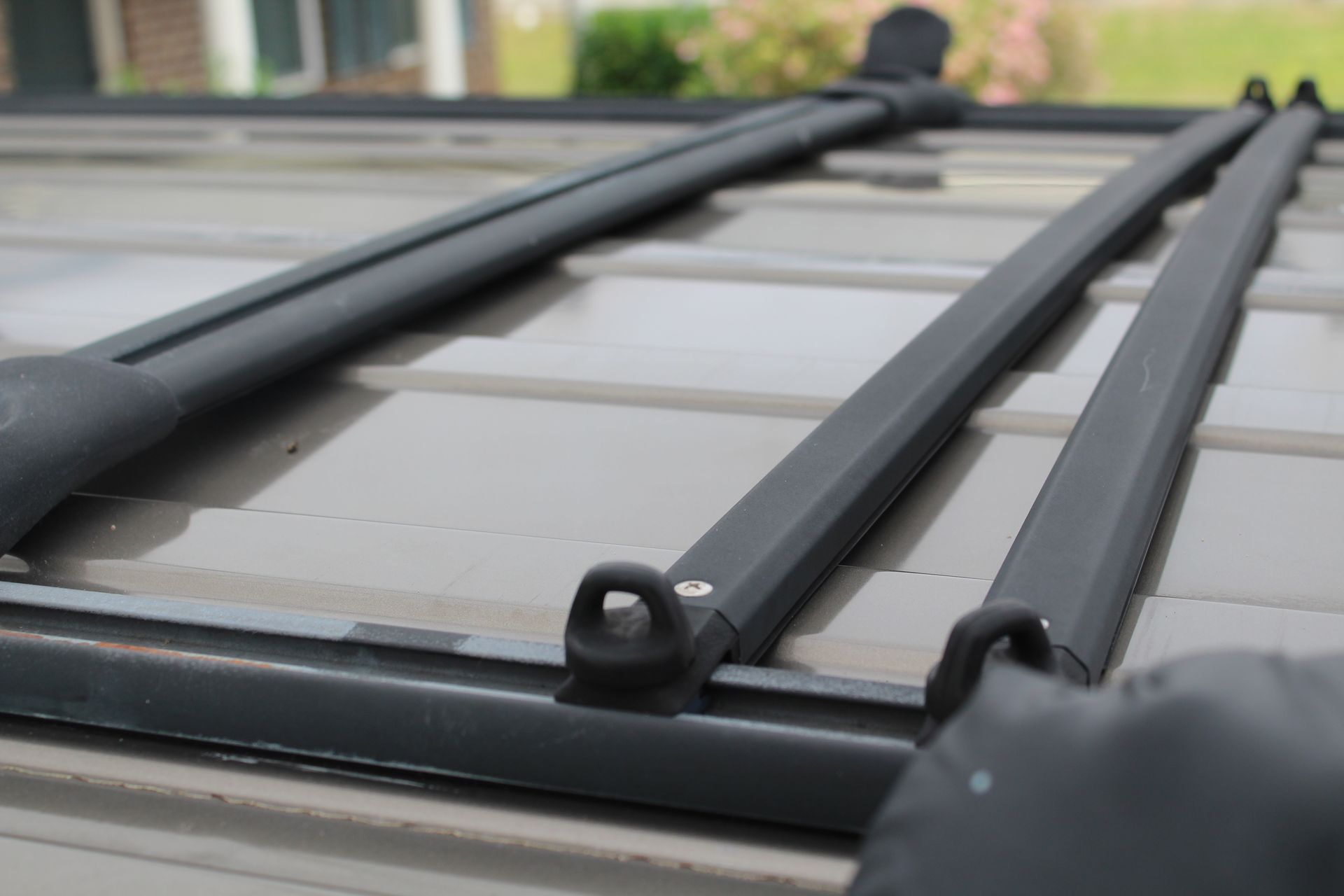 Black roof rack on a tan vehicle roof, with a loop for securing items.