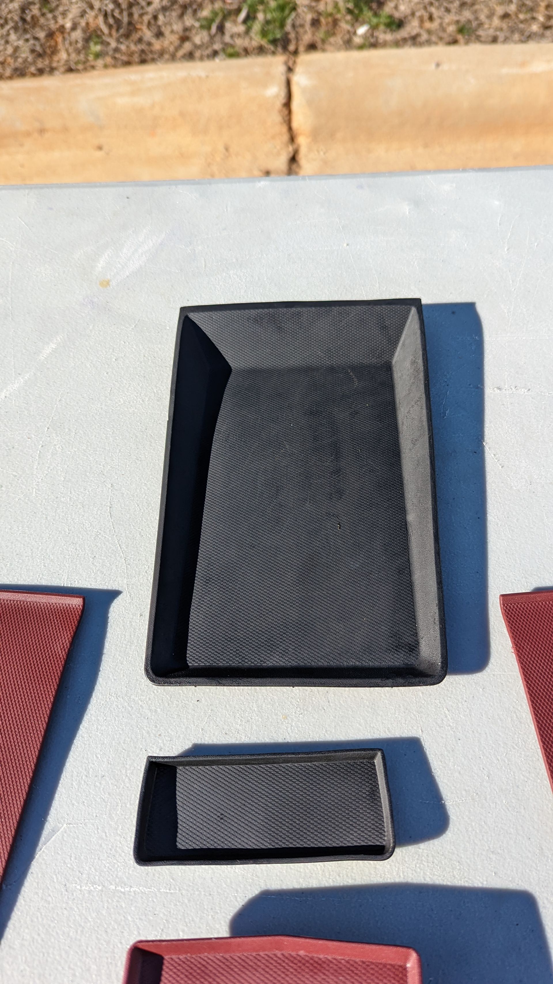 Black and red textured plastic trays on a gray surface outdoors.
