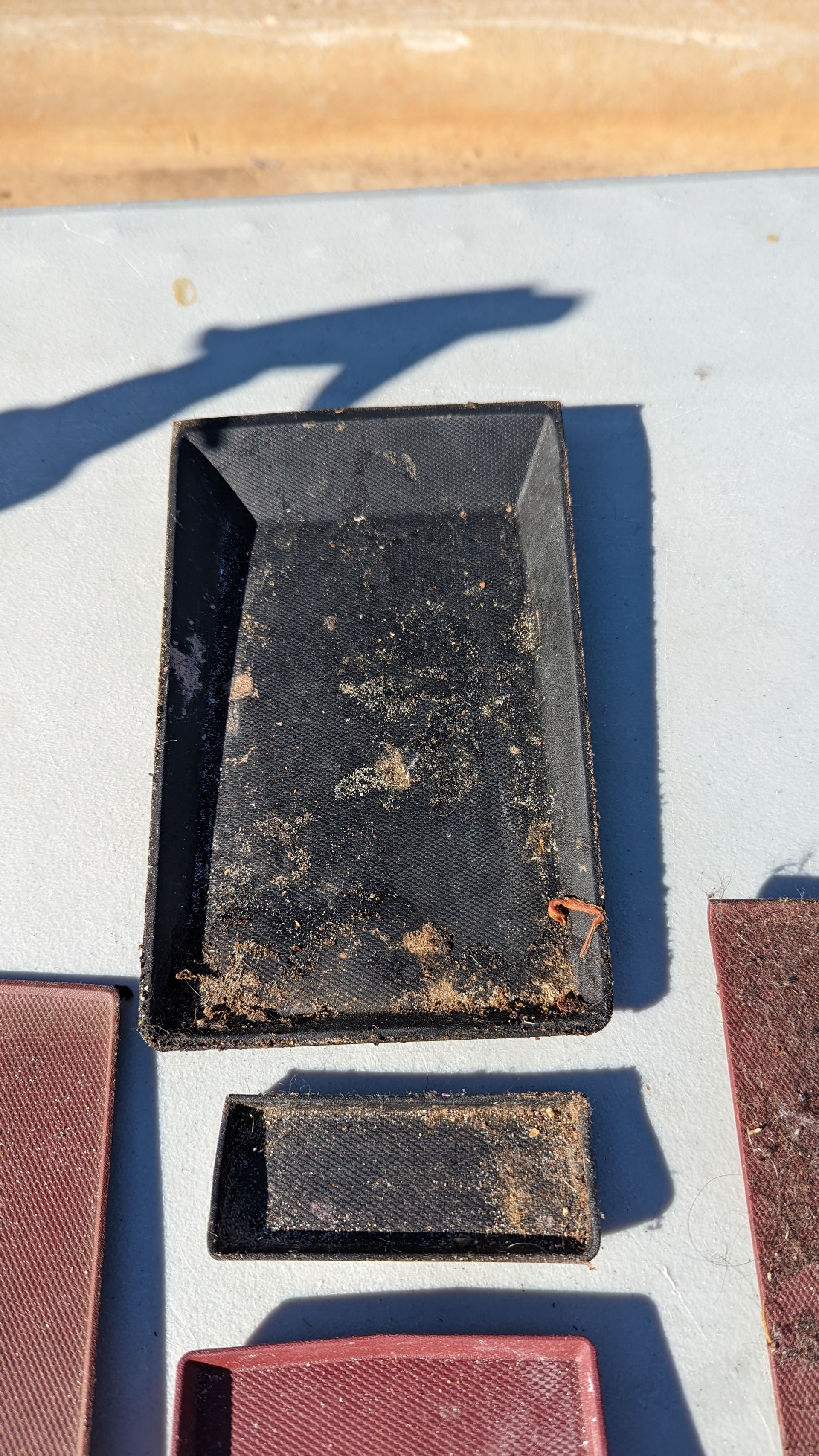 Black rectangular tray and smaller box, possibly for seedlings, on a light surface with shadows.