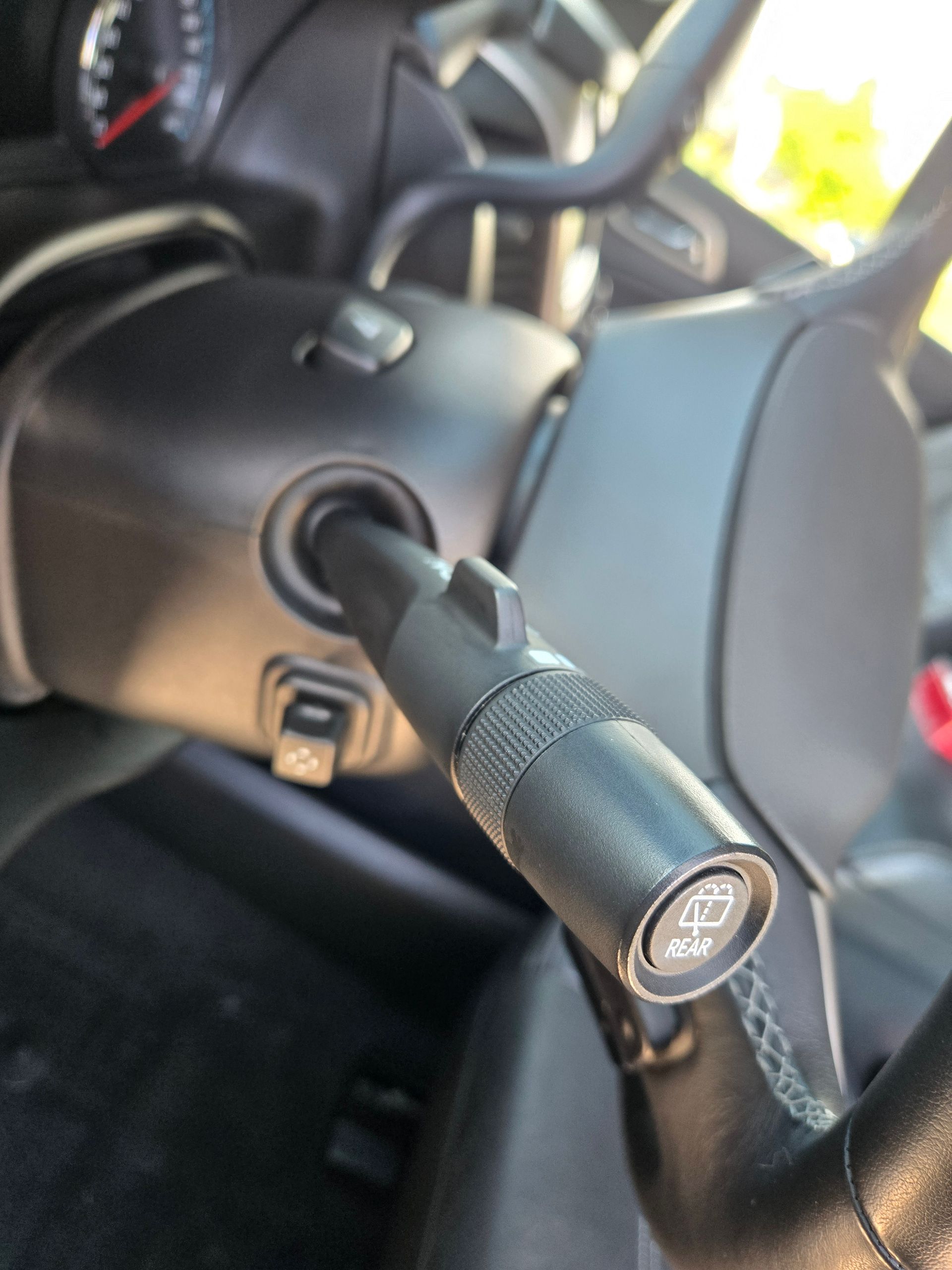 Close-up of car's black windshield wiper lever with wiper spray symbol near steering wheel.
