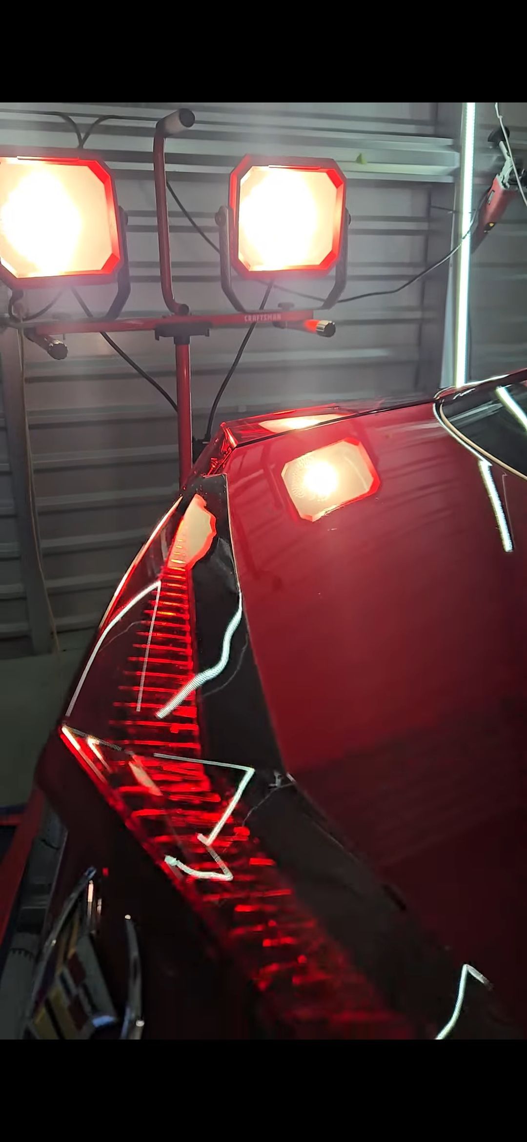 Red car tail light illuminated by overhead lights in a garage.