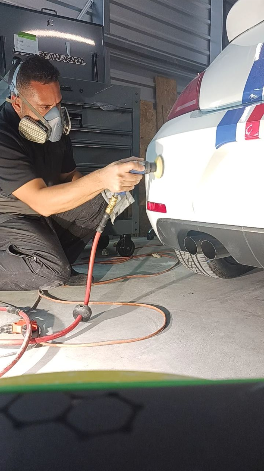 Person polishing a white car panel with an electric polisher; black gloves and tool.