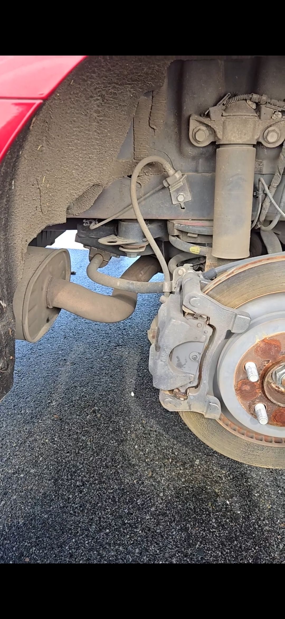 Car's rear suspension: brake caliper, rotor, shock absorber, and suspension components. Mud is visible on the car parts.