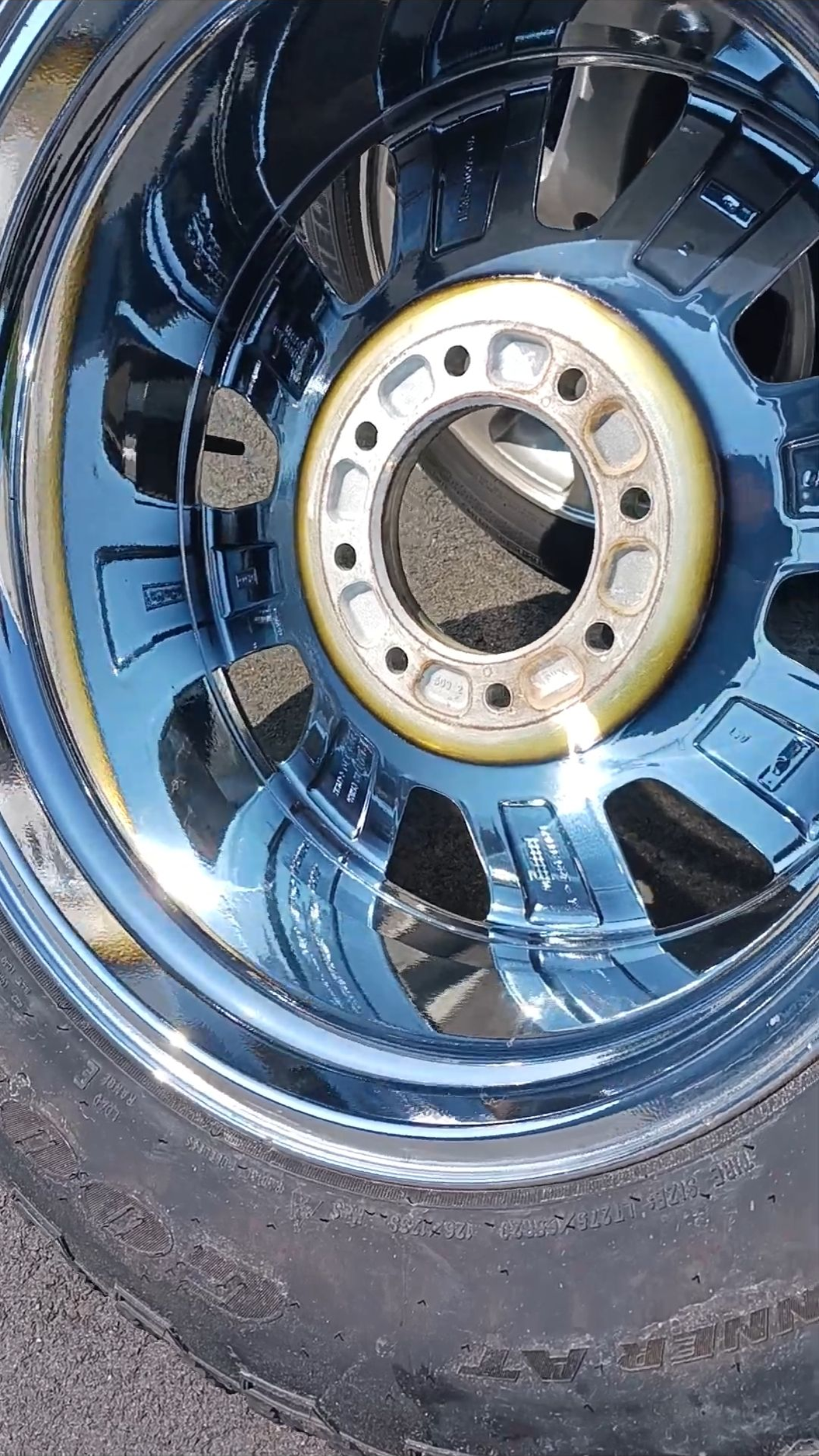 Close-up of a shiny blue and chrome car wheel, reflecting the surroundings, with a worn tire visible.