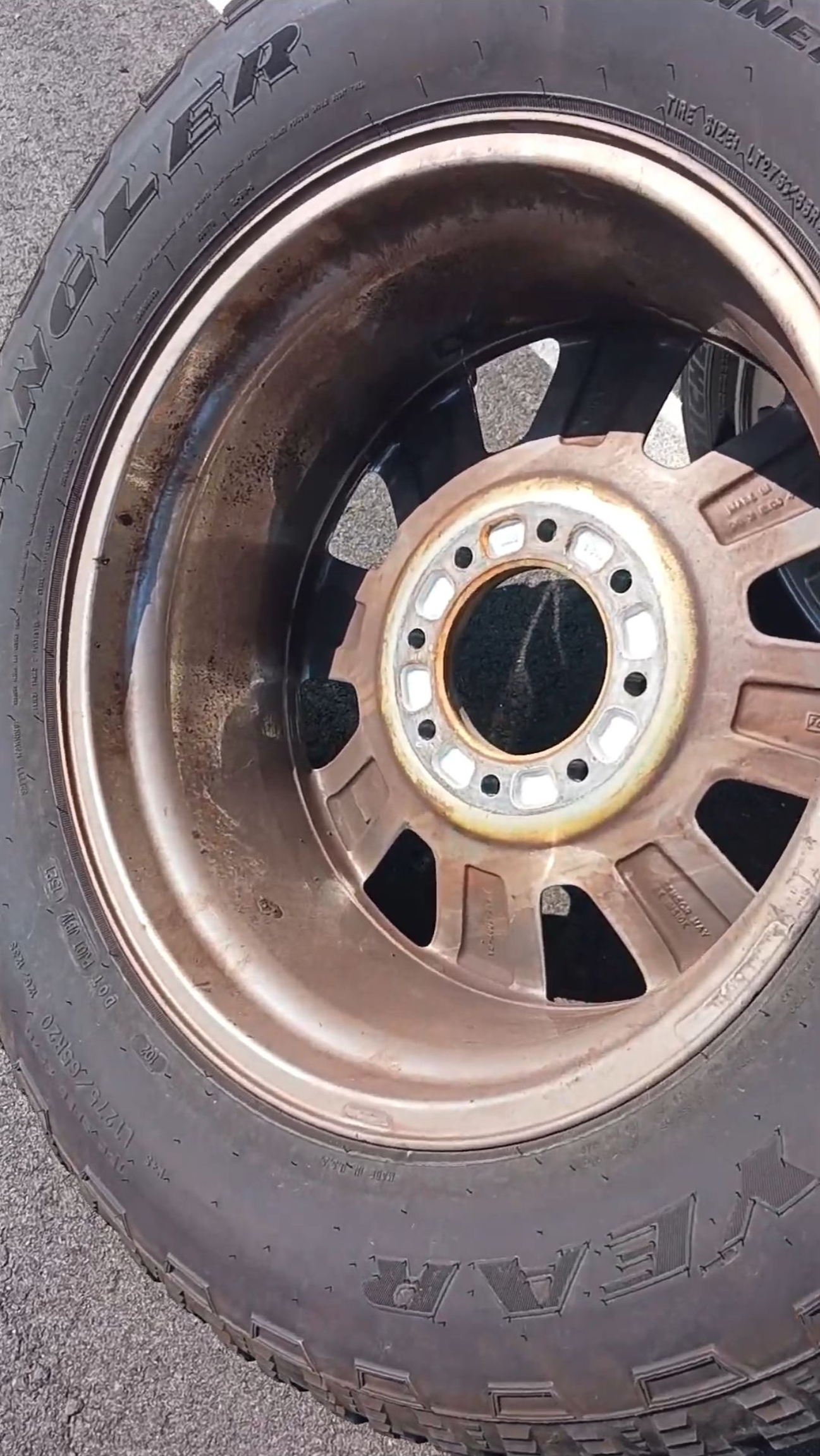 A dirty car wheel with a brown rim and a black tire on an outdoor surface.