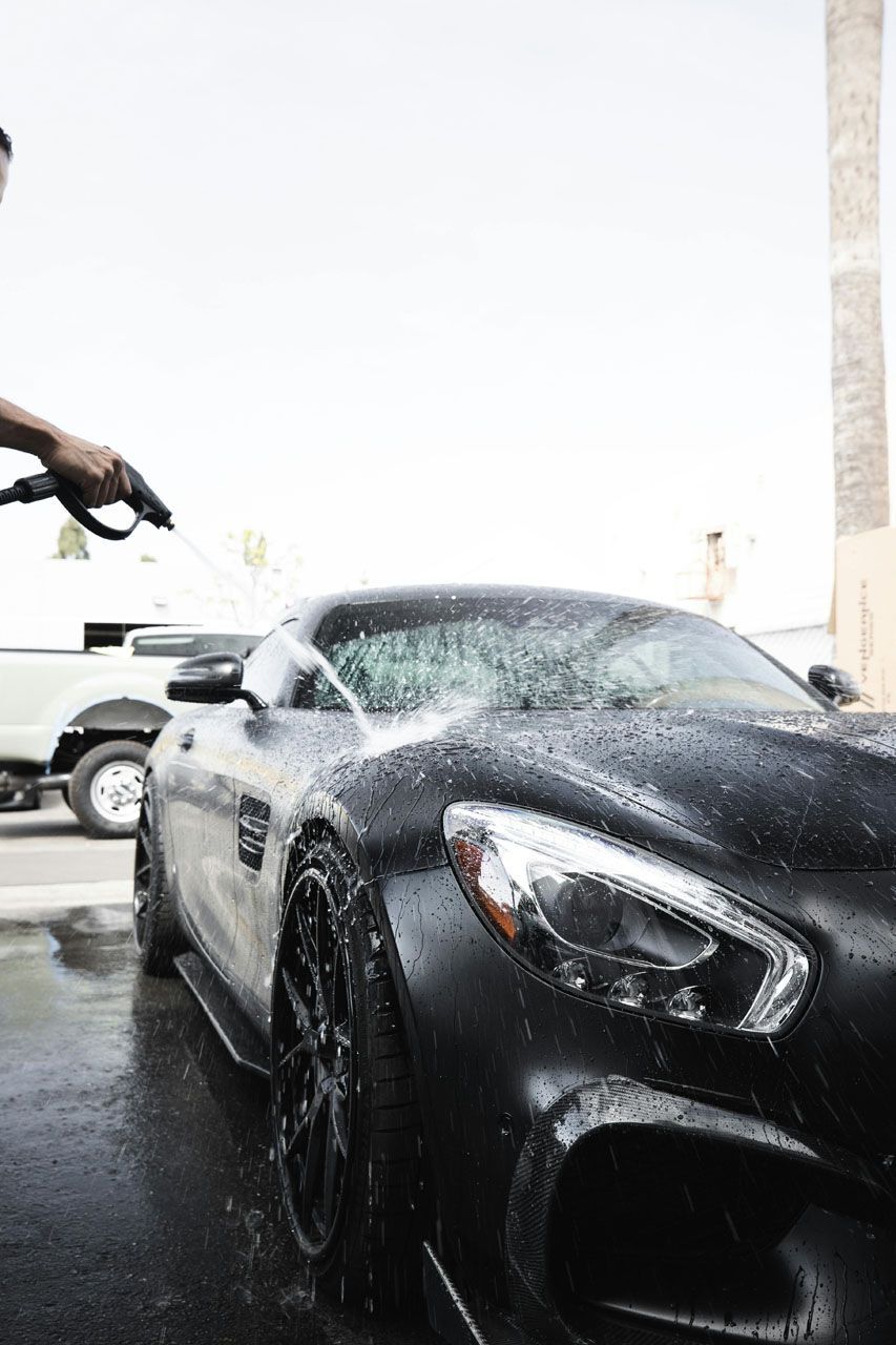 Man washing a black car with a sponge in a garage.