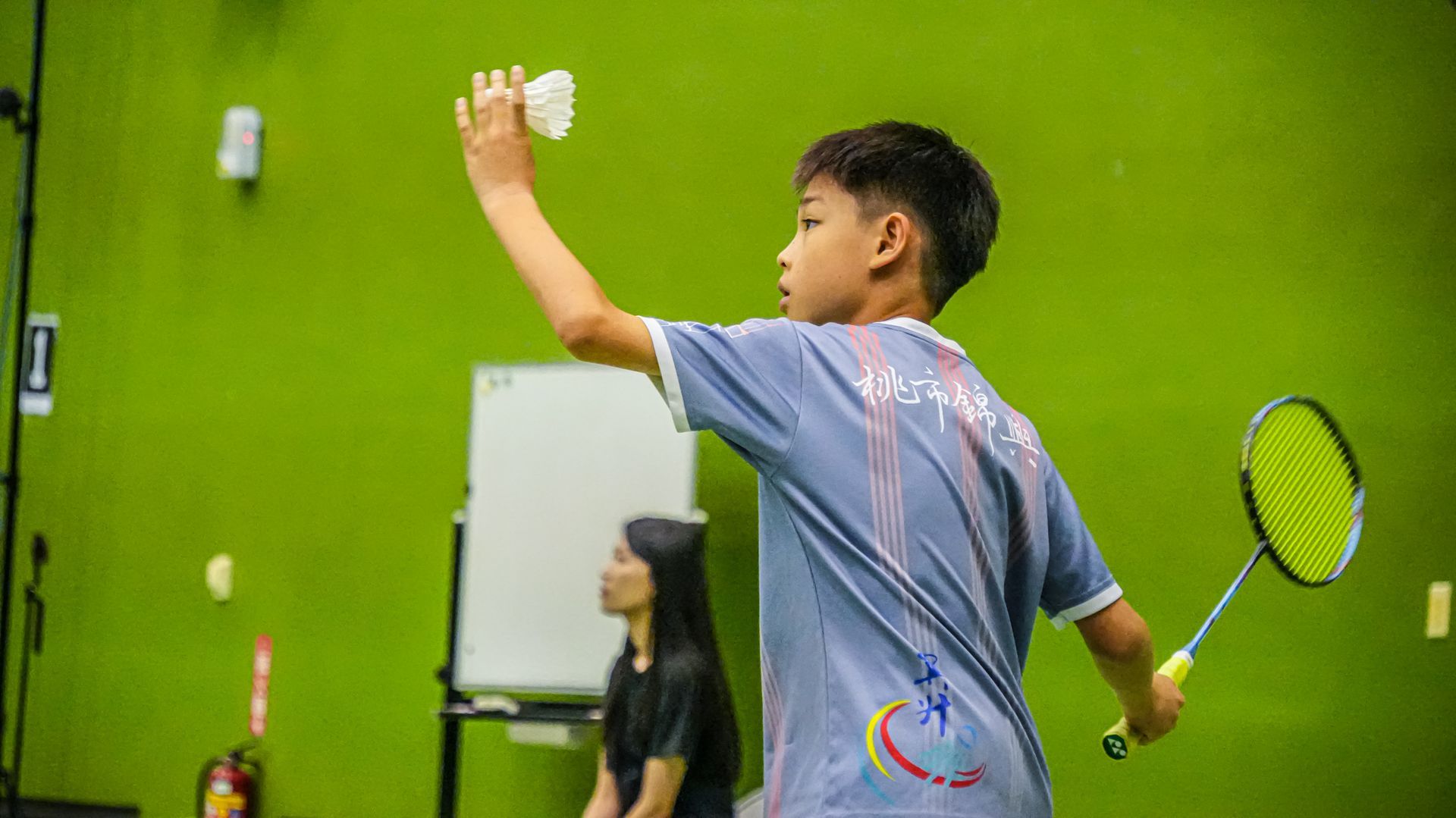 一個小男孩在綠色的牆前拿著羽毛球拍。