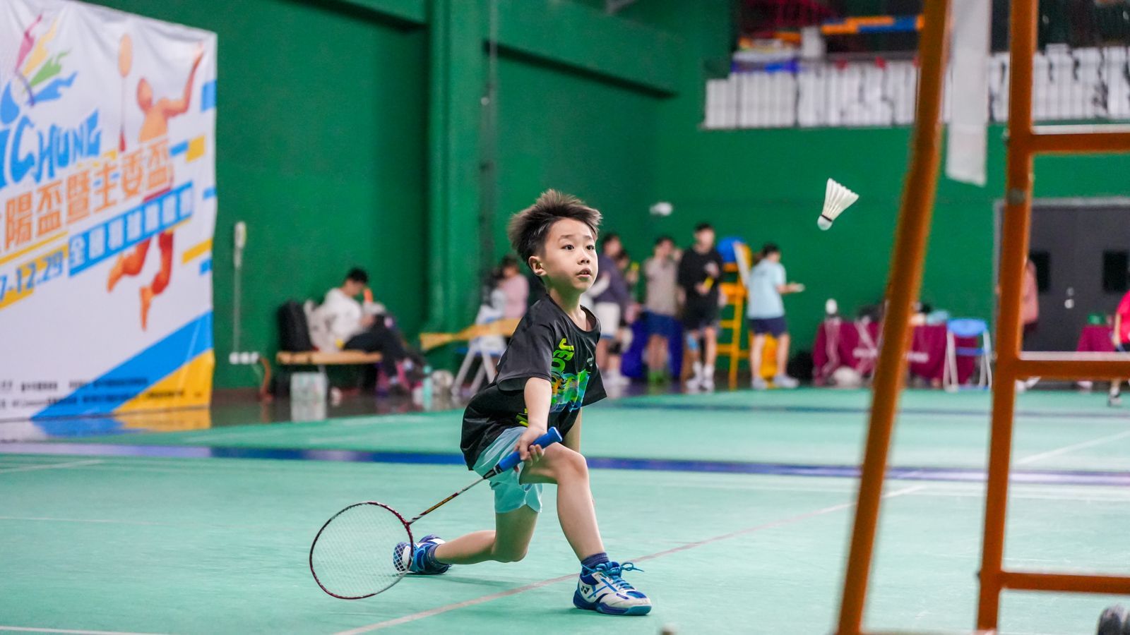 一個小男孩正在球場上打羽球。