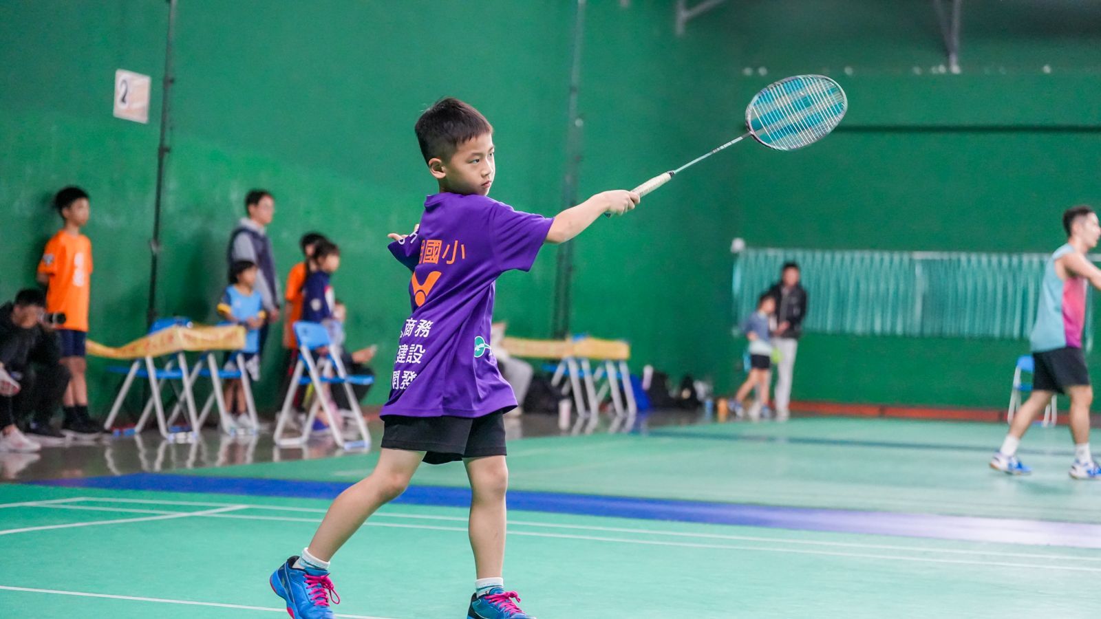 一個小男孩拿著羽球拍在球場上。