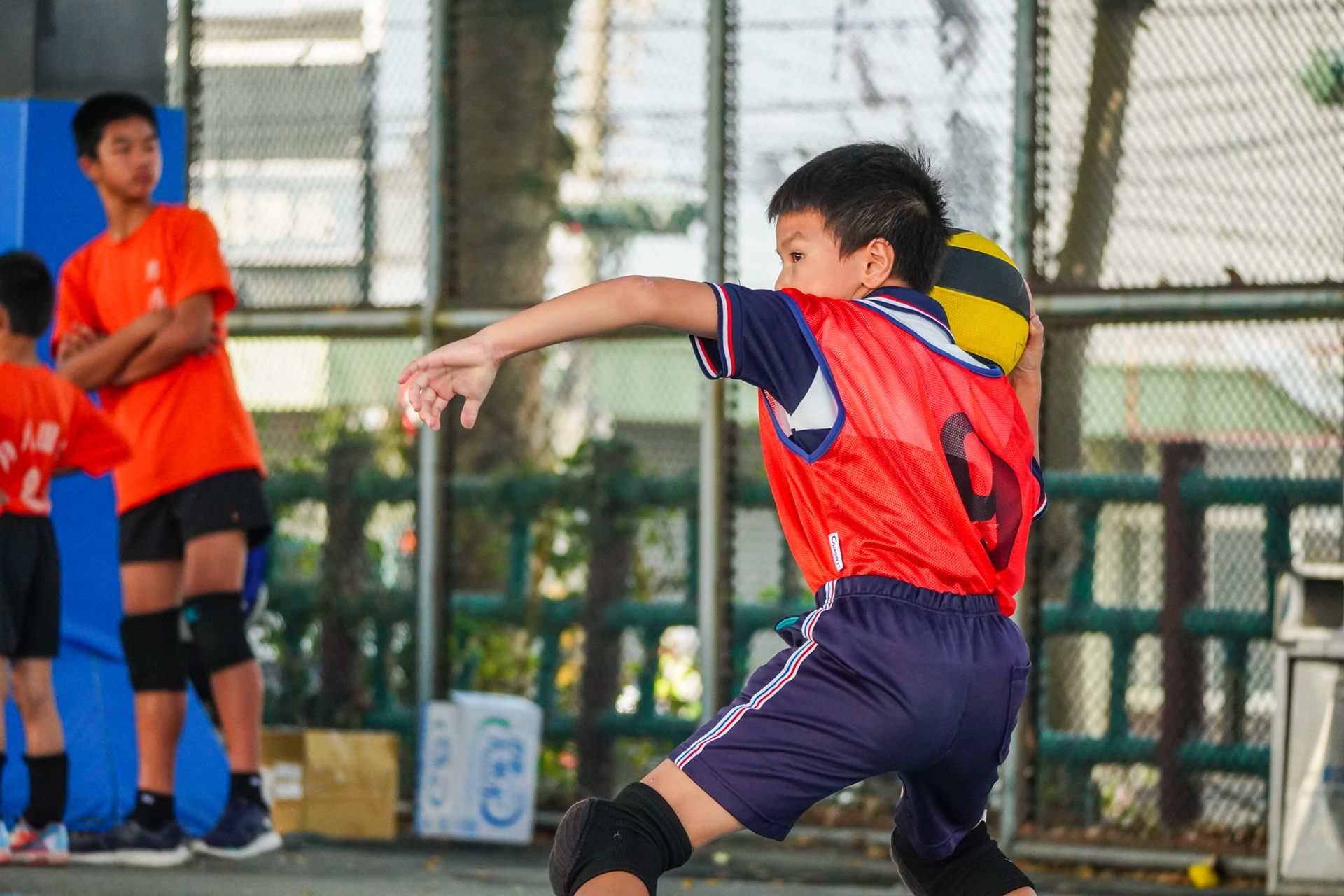 一個穿著紅色襯衫的小男孩正在球場上打排球。