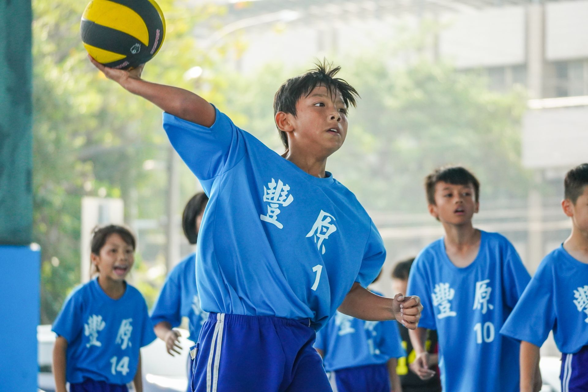 一個穿著藍色襯衫的男孩手裡拿著一個排球。