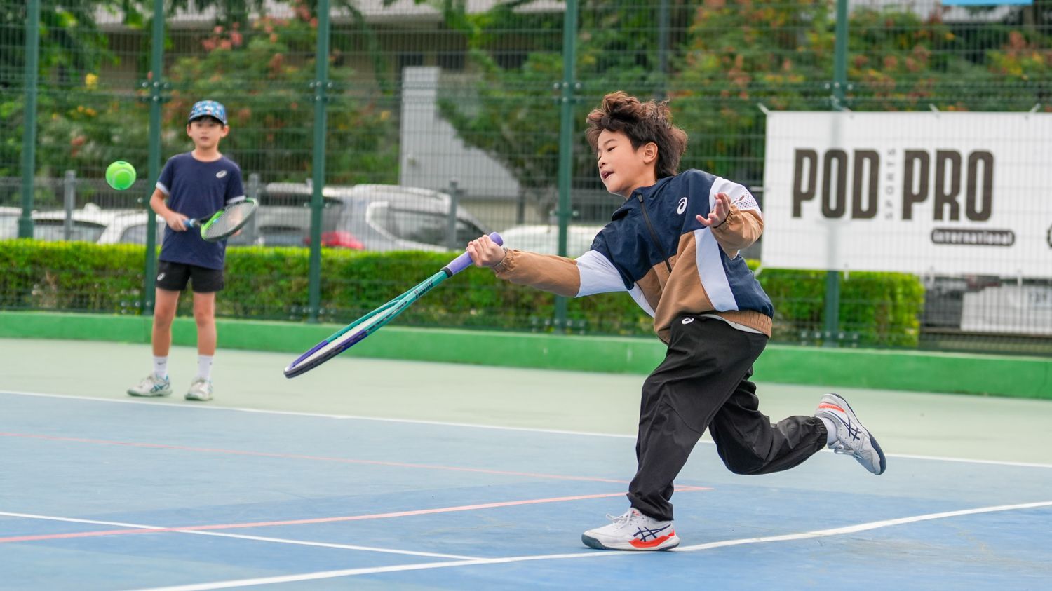 兩個小男孩正在網球場上打網球。