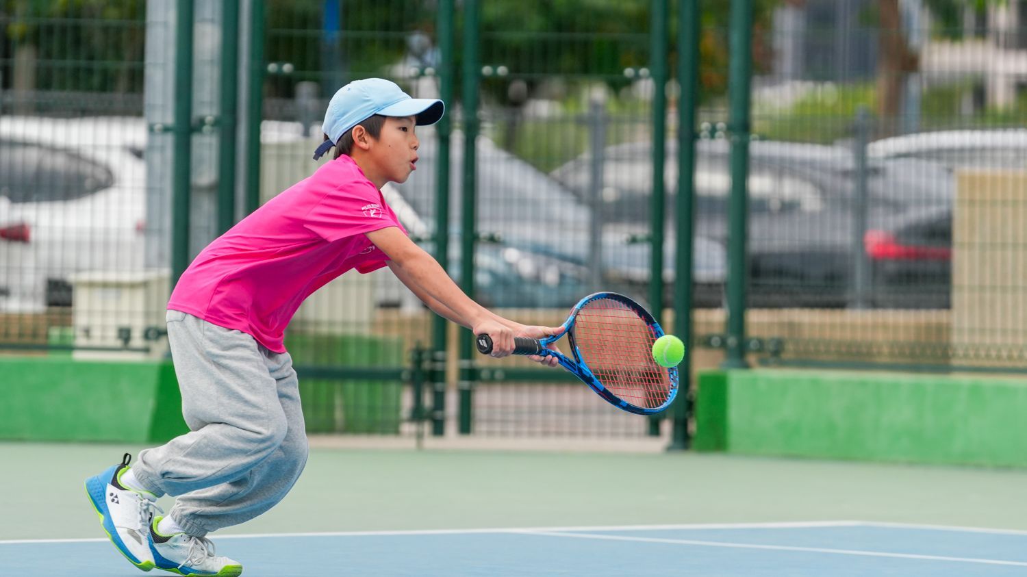 一個小男孩正在網球場上打網球。