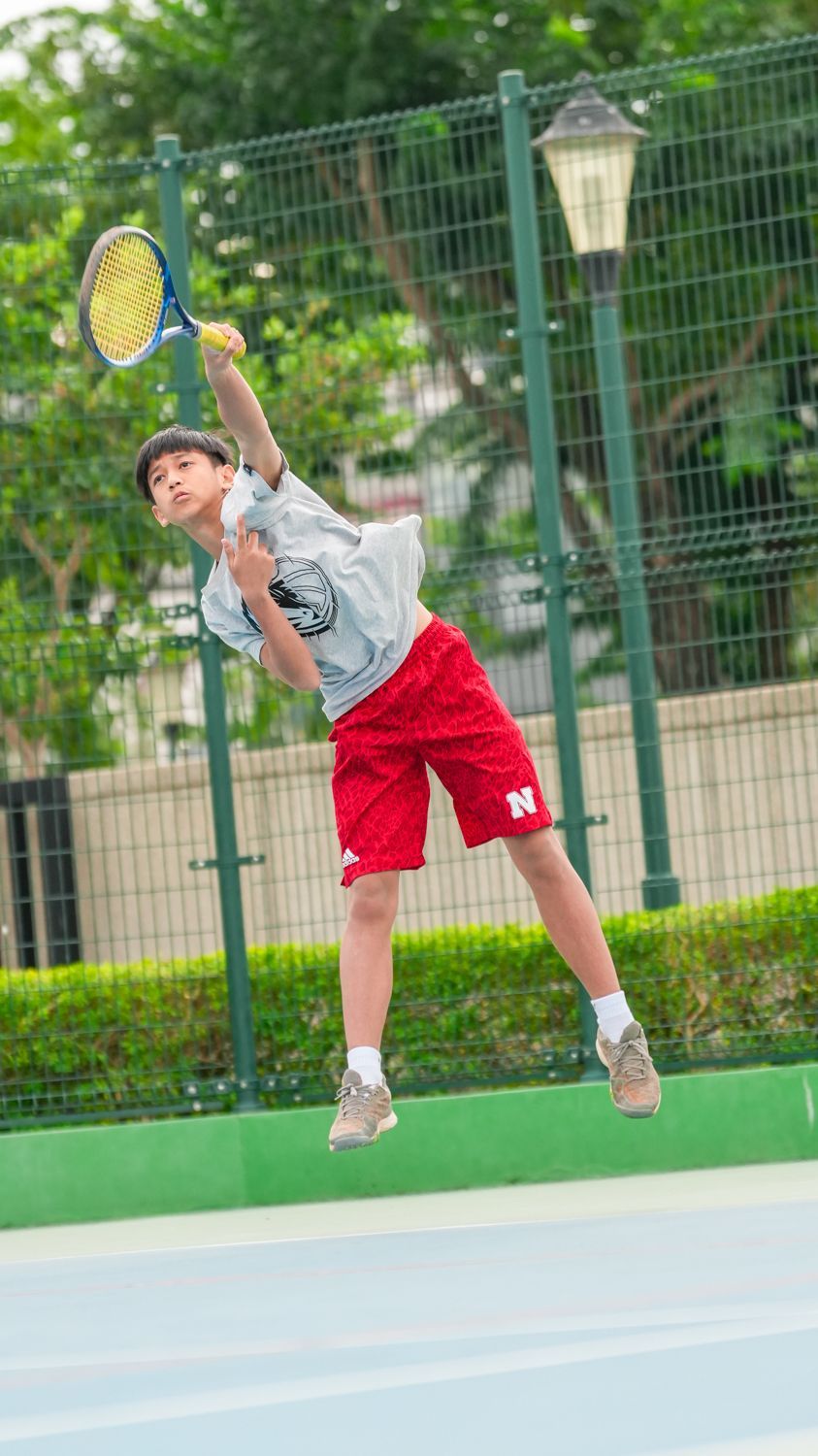 一個小男孩正在網球場上發網球。