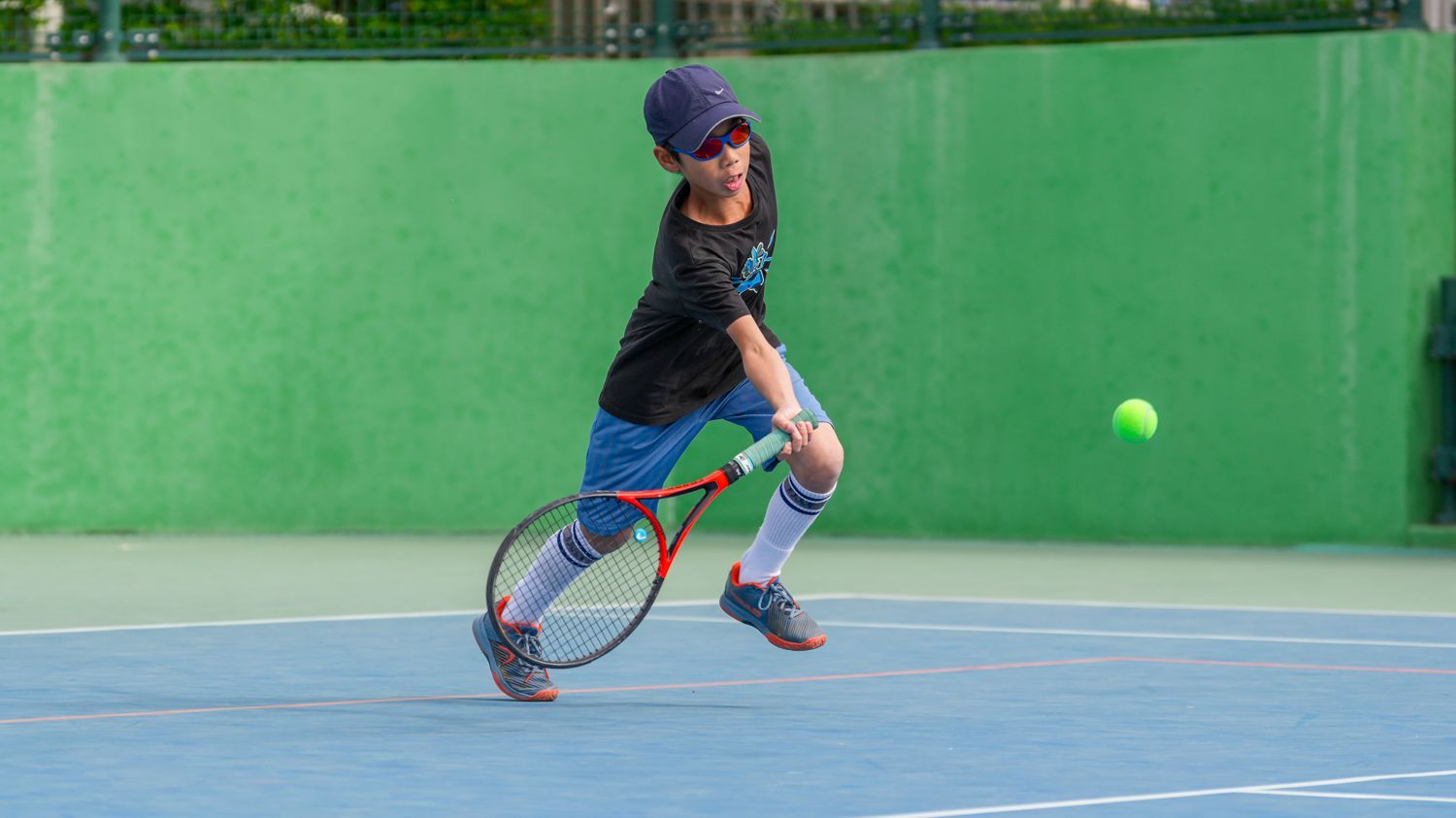 一個小男孩正在網球場上打網球。