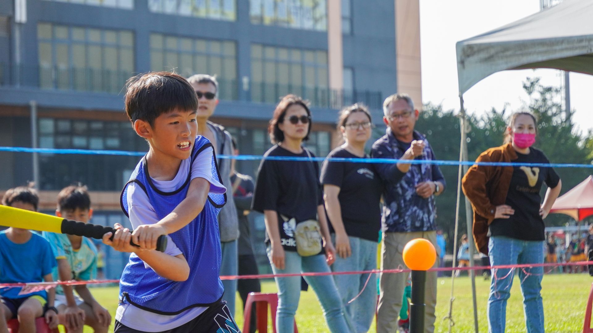 一個小男孩在球上揮舞球棒，人們在一旁觀看。