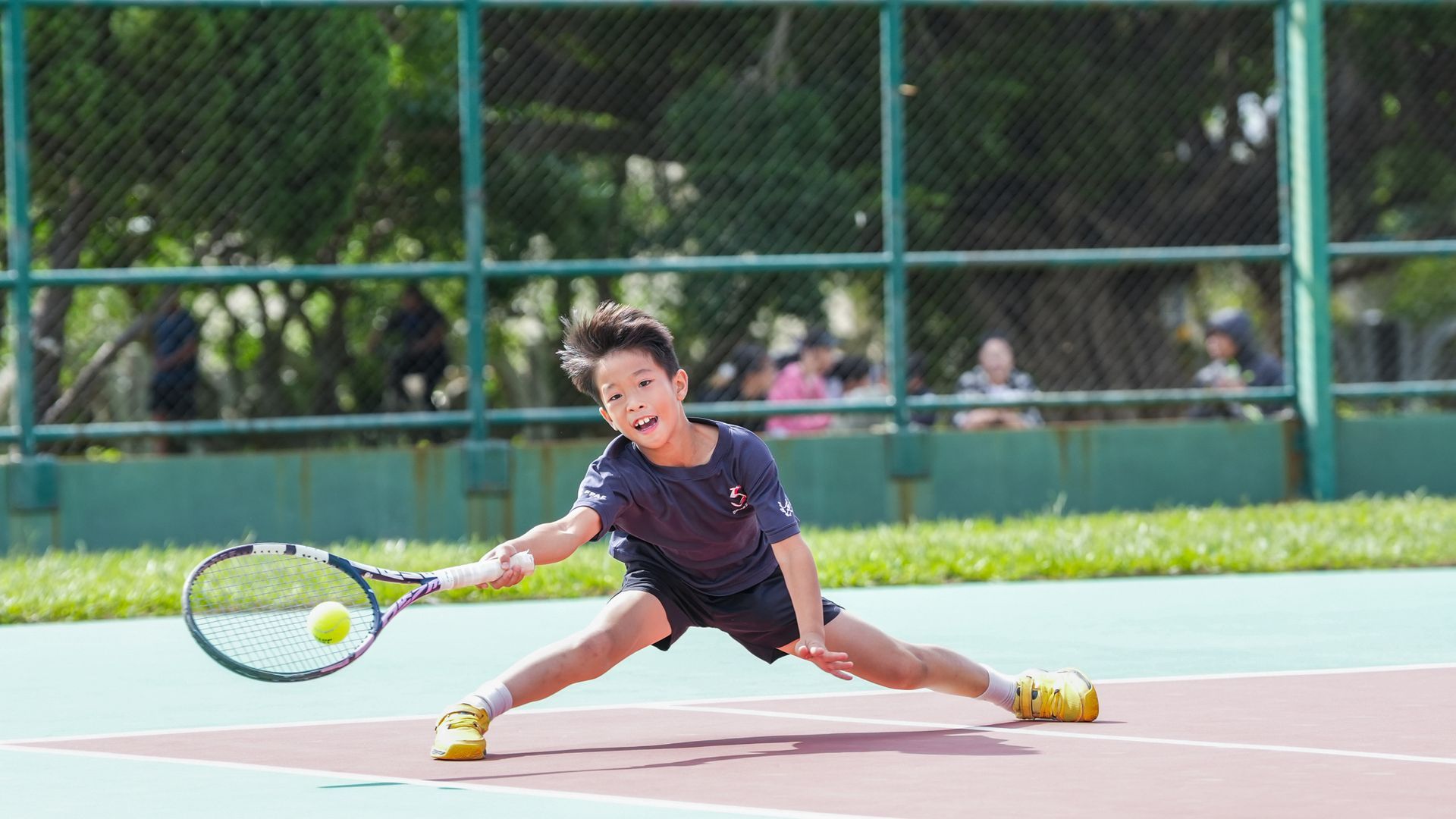 一個小男孩正在網球場上打網球。