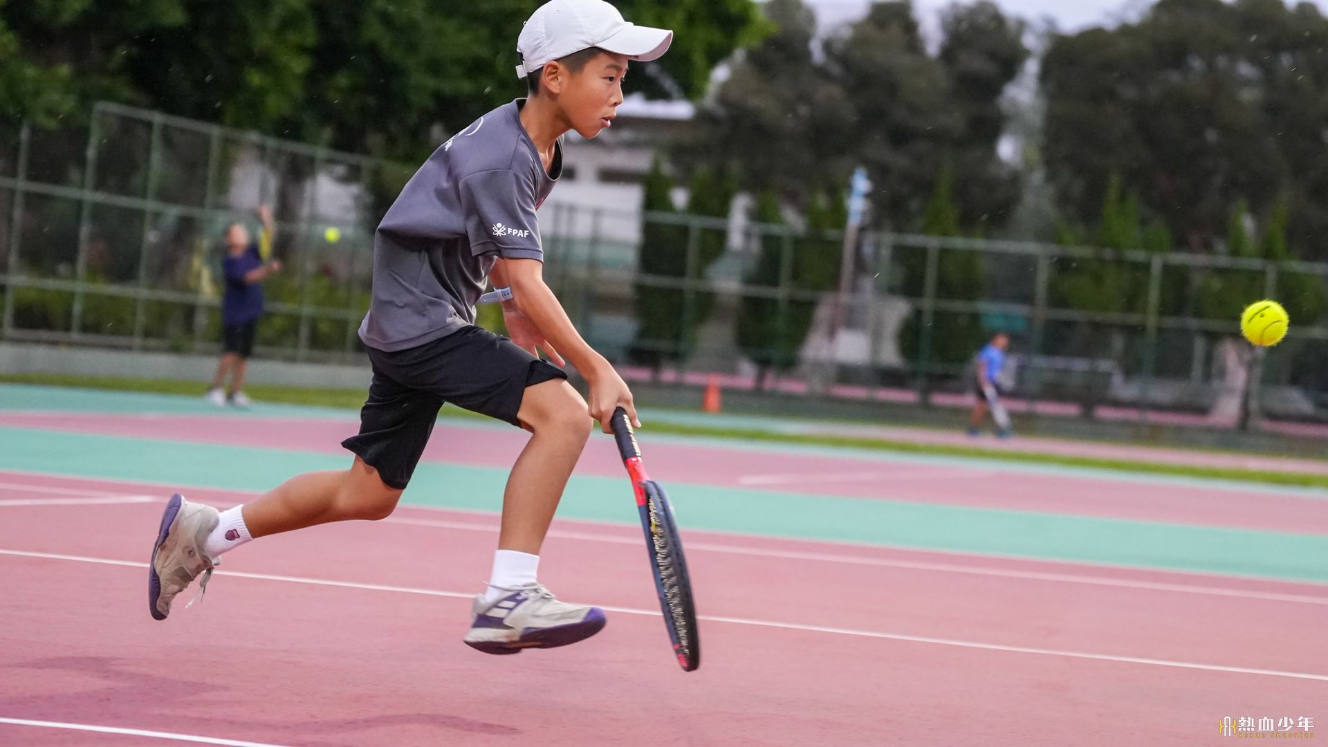 一個小男孩正在網球場上打網球。