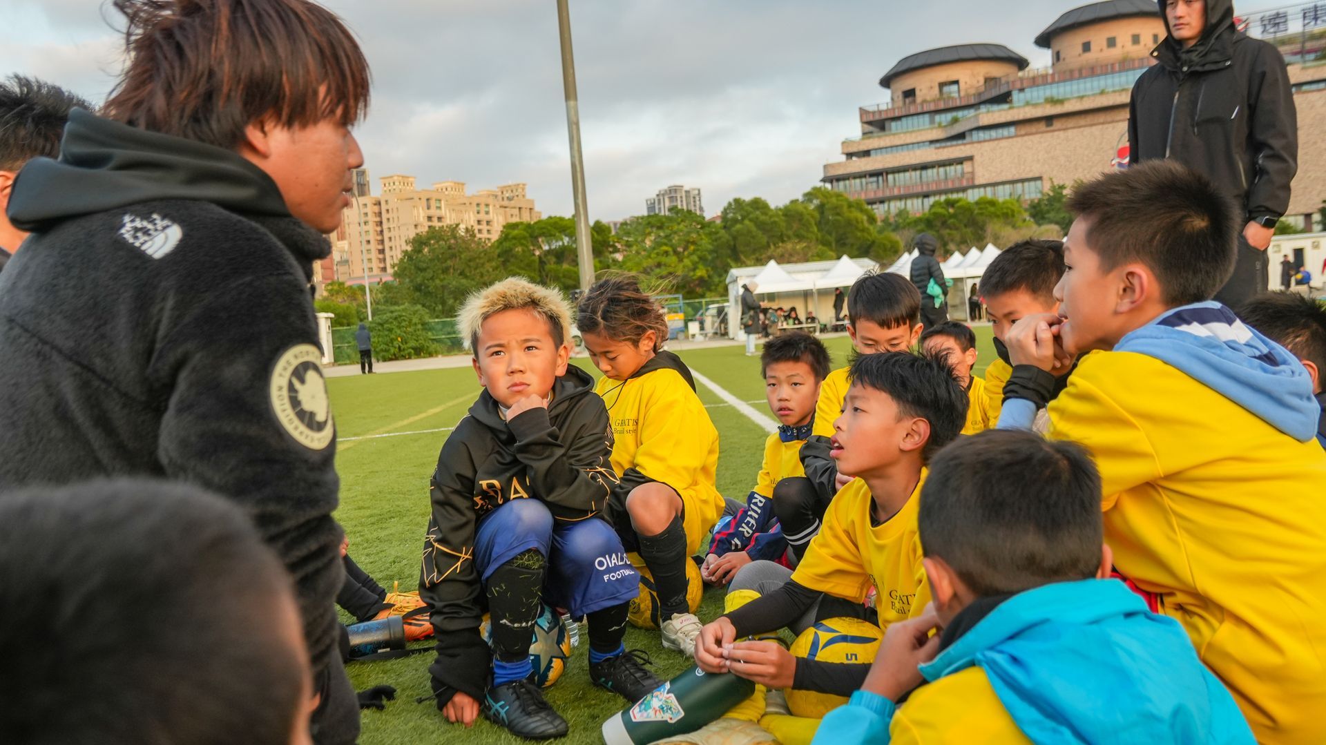 一名婦女正在足球場上與一群小男孩交談。