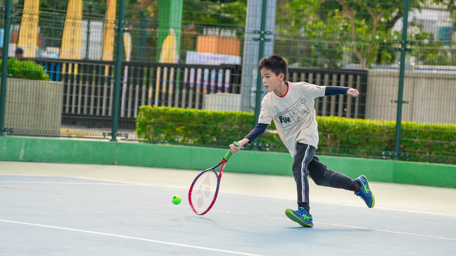 一個小男孩正在網球場上打網球。