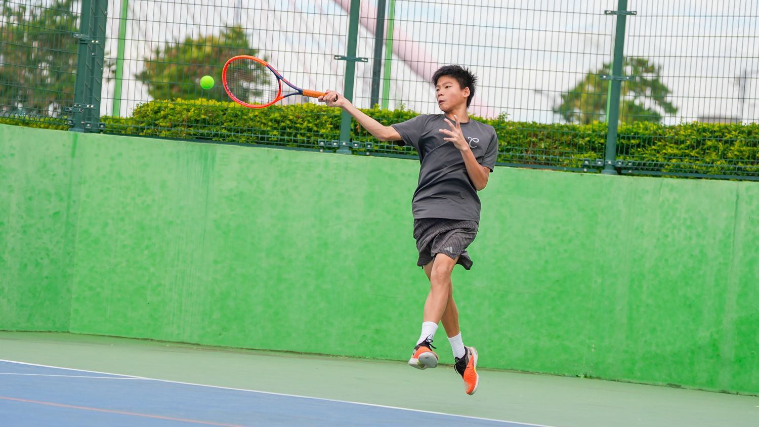 一個小男孩正在網球場上打網球。