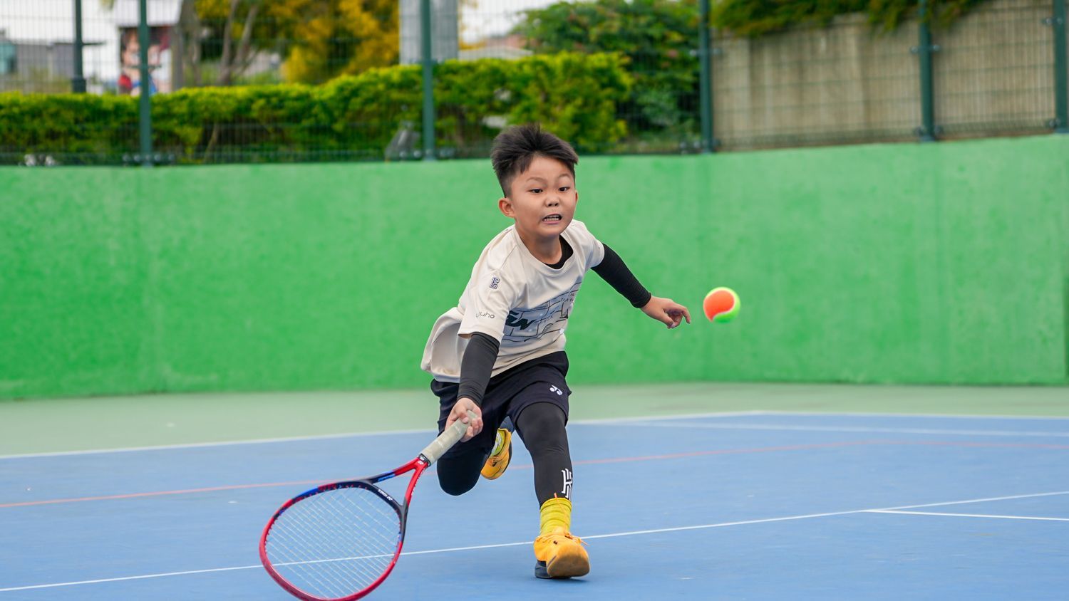 一個小男孩正在網球場上打網球。