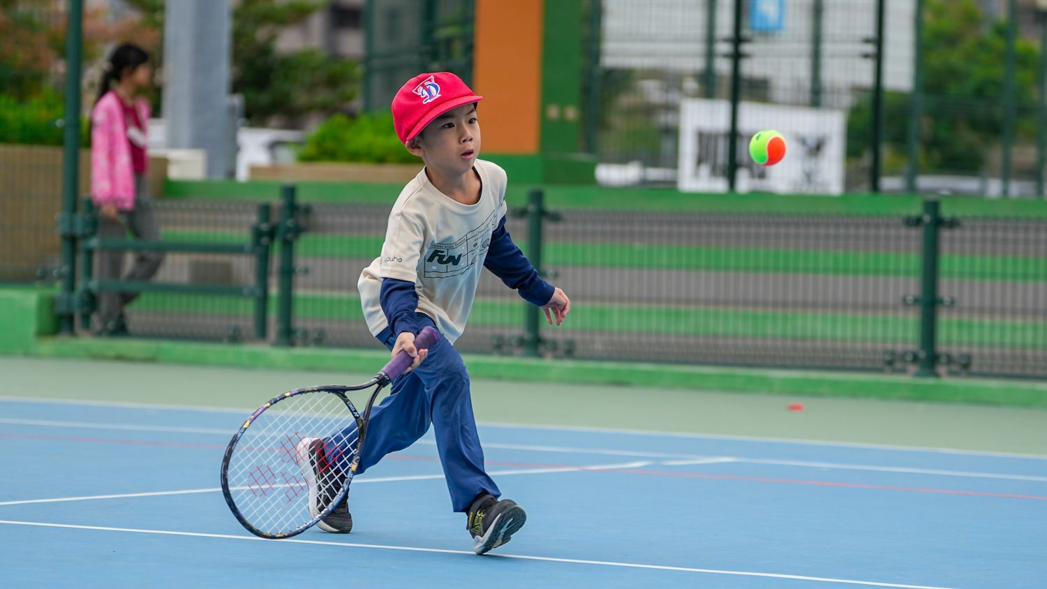 一個小男孩正在網球場上打網球。