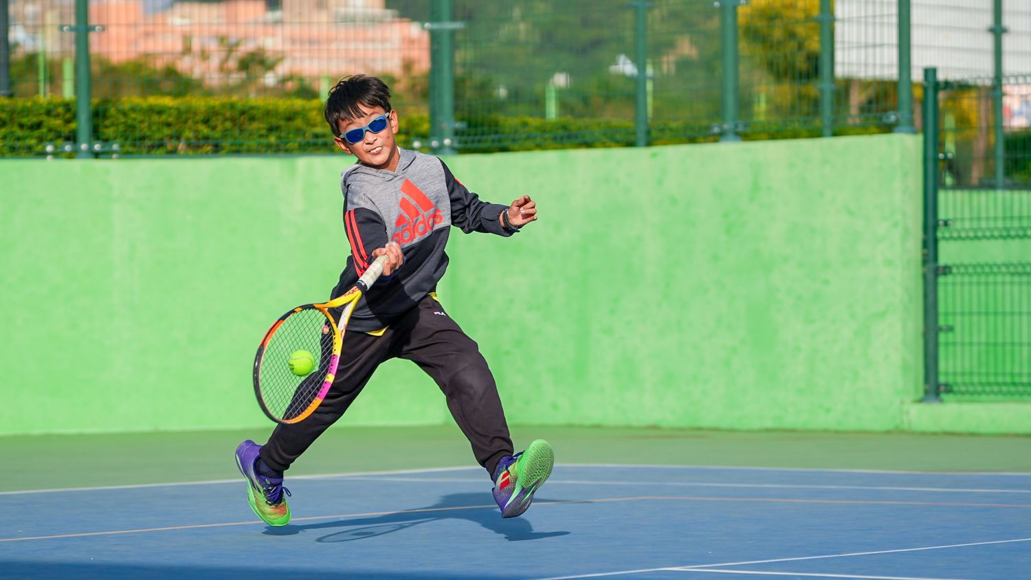 一個小男孩正在網球場上打網球。