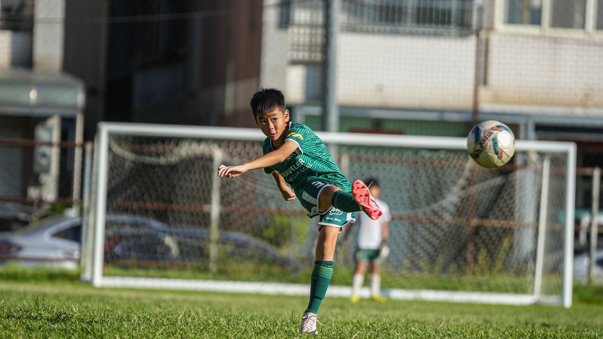 一個小男孩正在球場上踢足球。