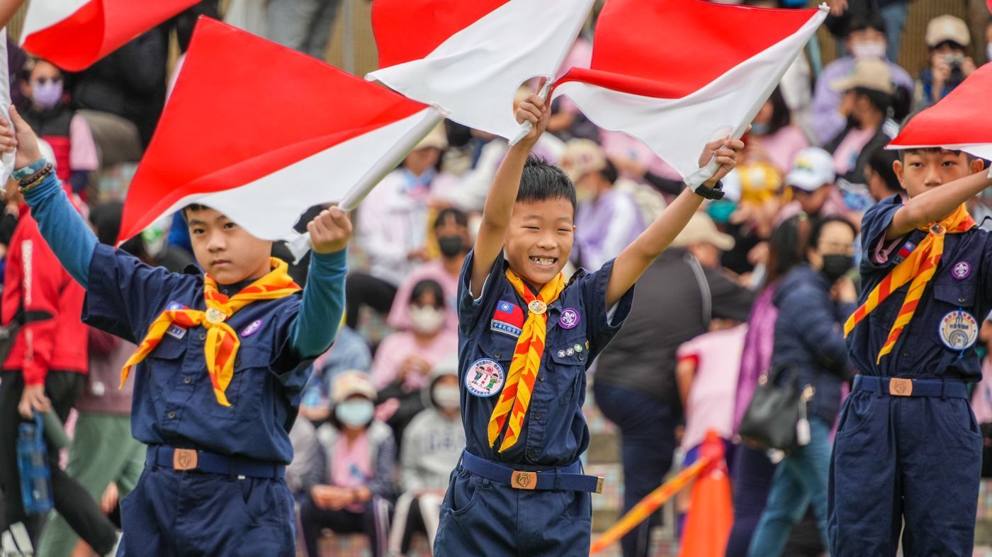 一群童子軍在人群面前舉著旗幟。